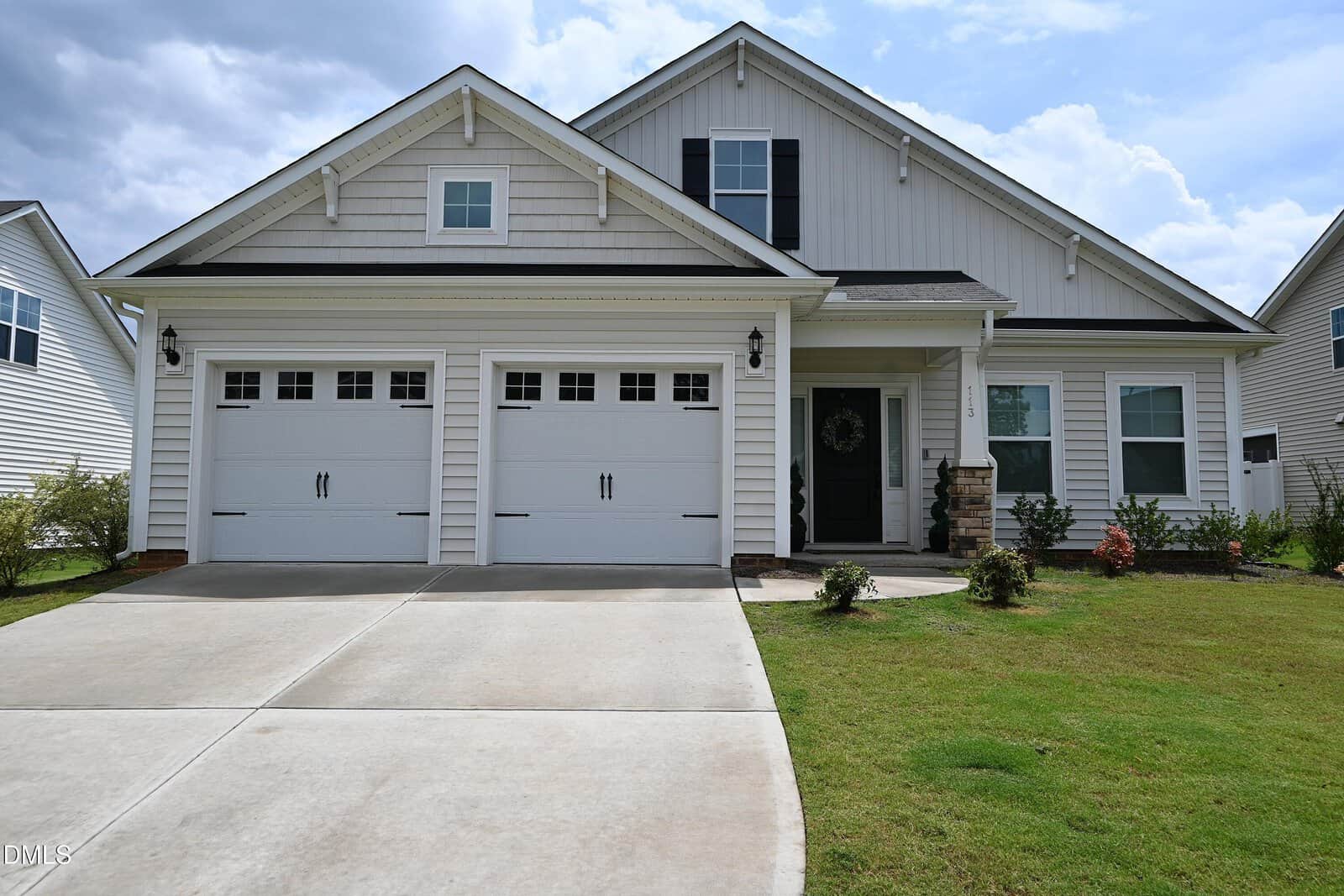 A modern white house at 113 Sugarmaple Way in Youngsville features two garage doors, black shutters, a covered entryway, and a well-kept lawn under a cloudy sky.
