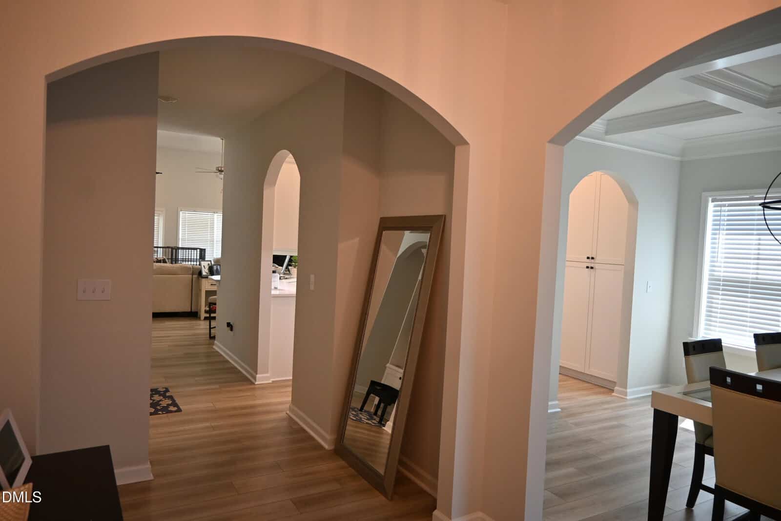 A hallway with light wood floors, arched doorways, a large mirror leaning against the wall, and a dining area with a table and chairs visible to the right.