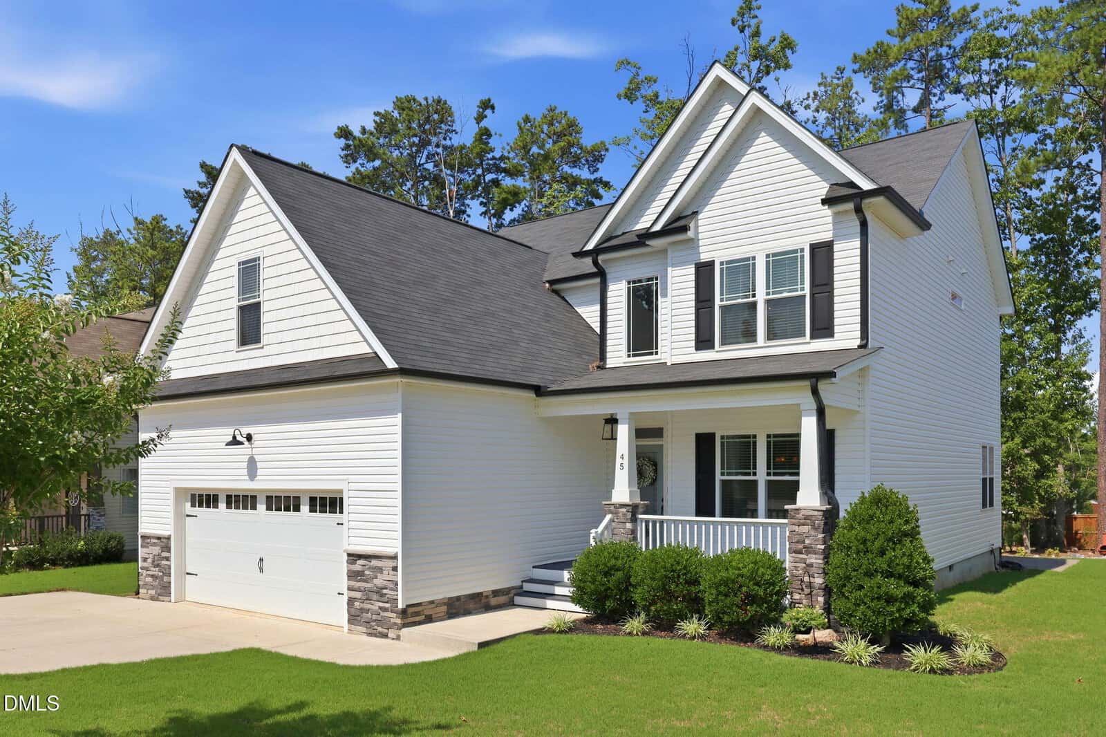 A modern two-story white house at 45 Kathleen Court, Youngsville, featuring black roof shingles, a double garage, front porch, and manicured green lawn surrounded by bushes and trees under a clear blue sky.