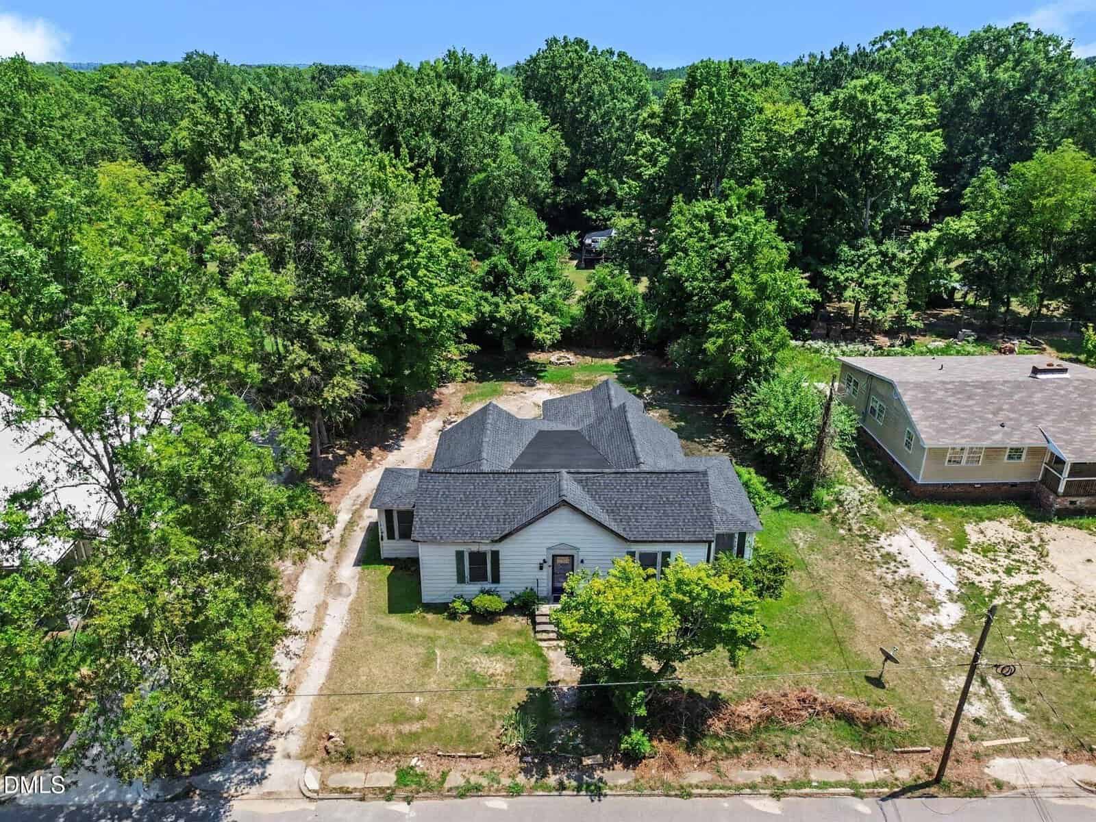 Aerial view of a single-story house with a dark roof at 418 E Green Street, Franklinton, surrounded by trees and greenery, with a yard in front and another home nearby under a blue sky.