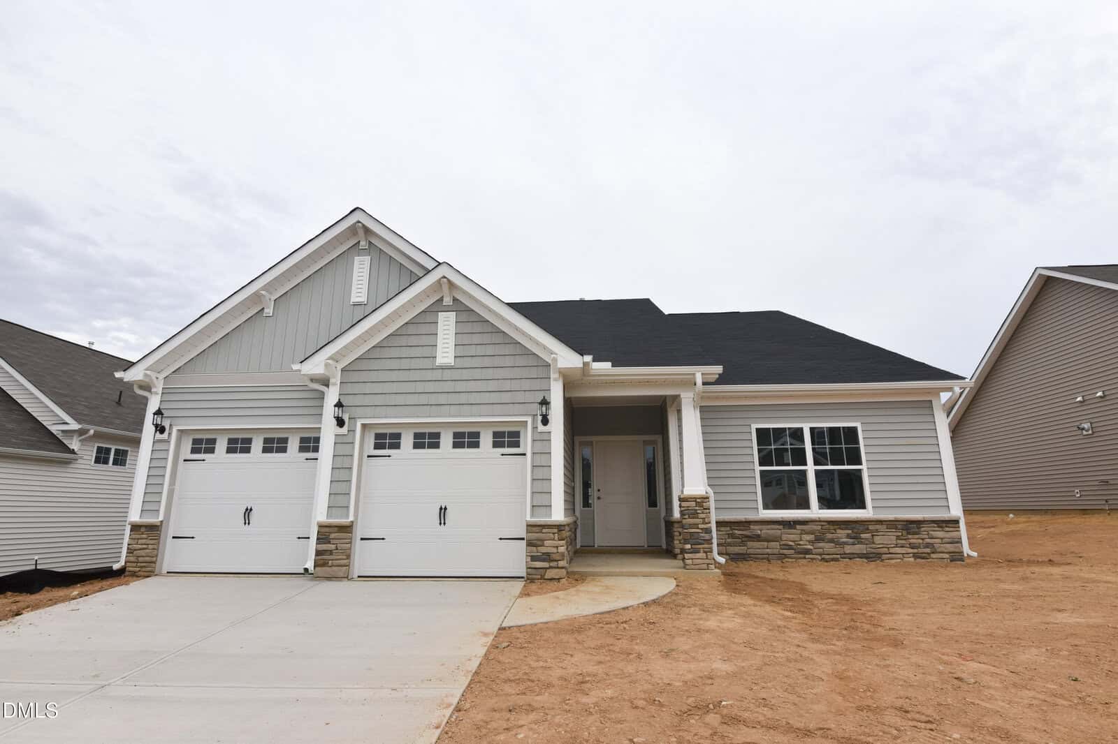 A new single-story house at 73 Moon Flower Walk in Youngsville features gray siding, two white garage doors, a covered entryway, and stone accents, surrounded by bare dirt and no landscaping.
