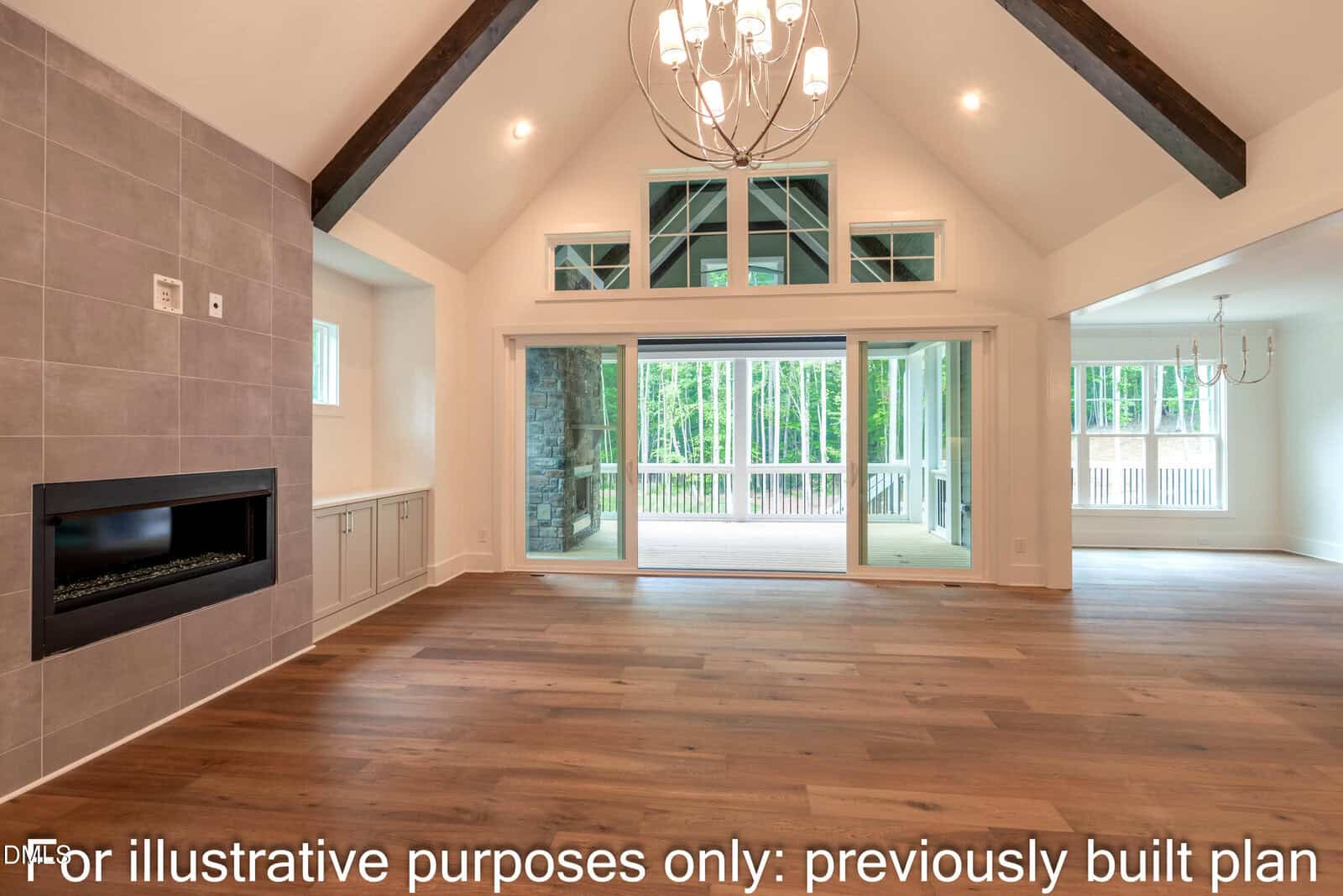 Spacious living room with vaulted ceiling, chandelier, modern fireplace, built-in cabinets, large windows, and sliding doors leading to a covered patio with wooded views. Text at bottom reads, “For illustrative purposes only: previously built plan.”.