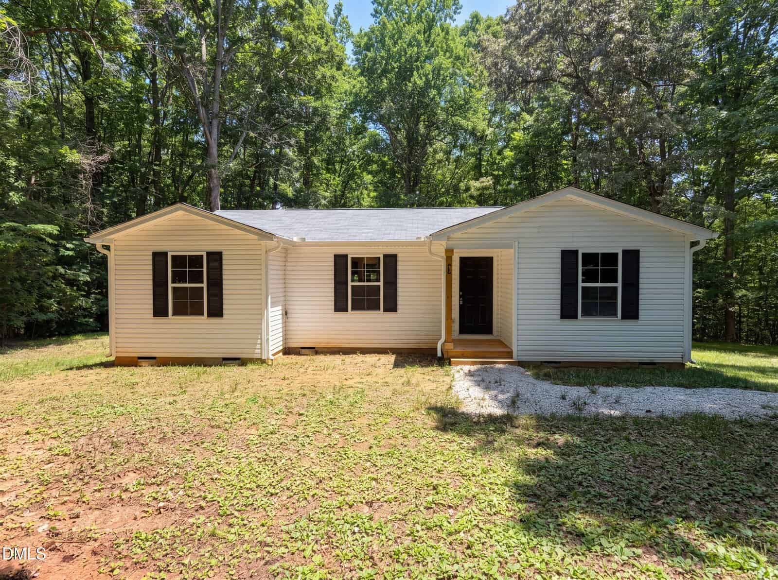 Single-story white house with black shutters and a dark front door, surrounded by trees at 25 Beechnut Court in Franklinton. It features a simple lawn with patches of grass and a small gravel area near the entrance.