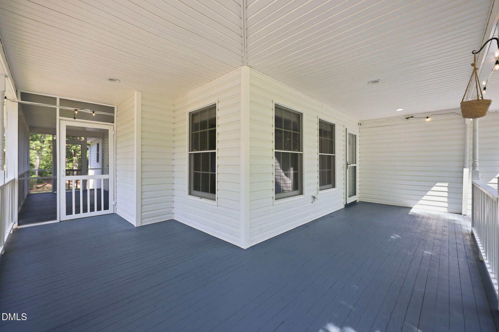 A spacious screened-in porch with white paneled walls and ceiling, dark blue wooden floor, several windows, and a door leading outside. The space is bright with natural light.