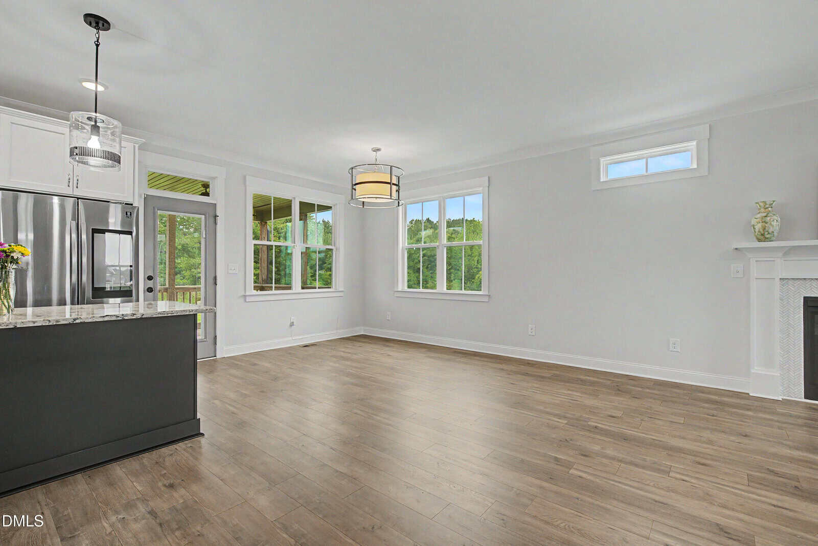 Bright, modern kitchen and living area with wood floors, white walls, large windows, stainless steel appliances, a small kitchen island, and a fireplace.