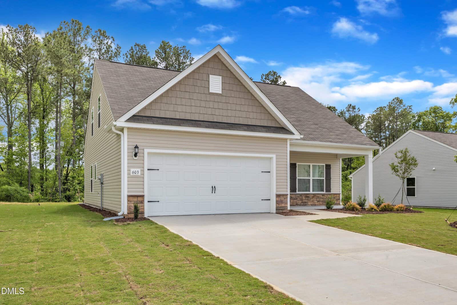 A modern single-story house with a gable roof, double garage, beige siding, and stone accents sits on a neat lawn under a blue sky with scattered clouds at 1109 Rhino Bend in Oxford.