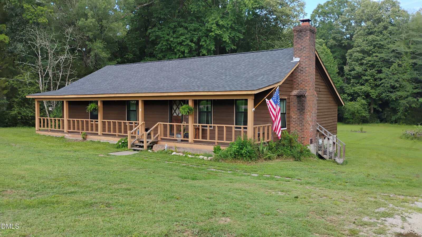 A brown wooden cabin at 959 Cheves Road in Zebulon features a large front porch, brick chimney, and American flag, surrounded by green grass and trees under a partly cloudy sky.