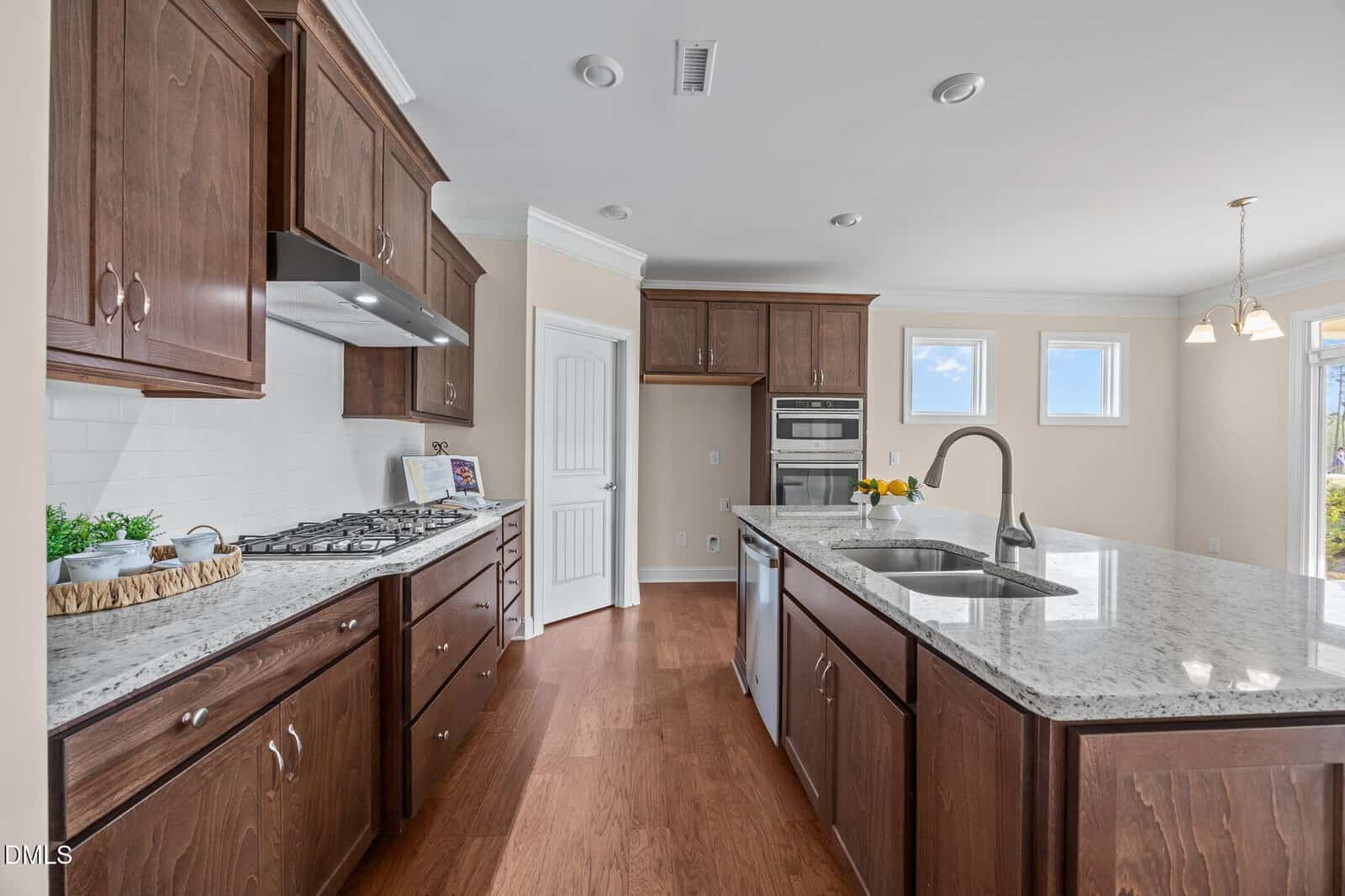 Modern kitchen with dark wood cabinets, stainless steel appliances, granite countertops, an island with a sink, and hardwood floors. Two windows provide natural light, and pendant lights hang over the island.
