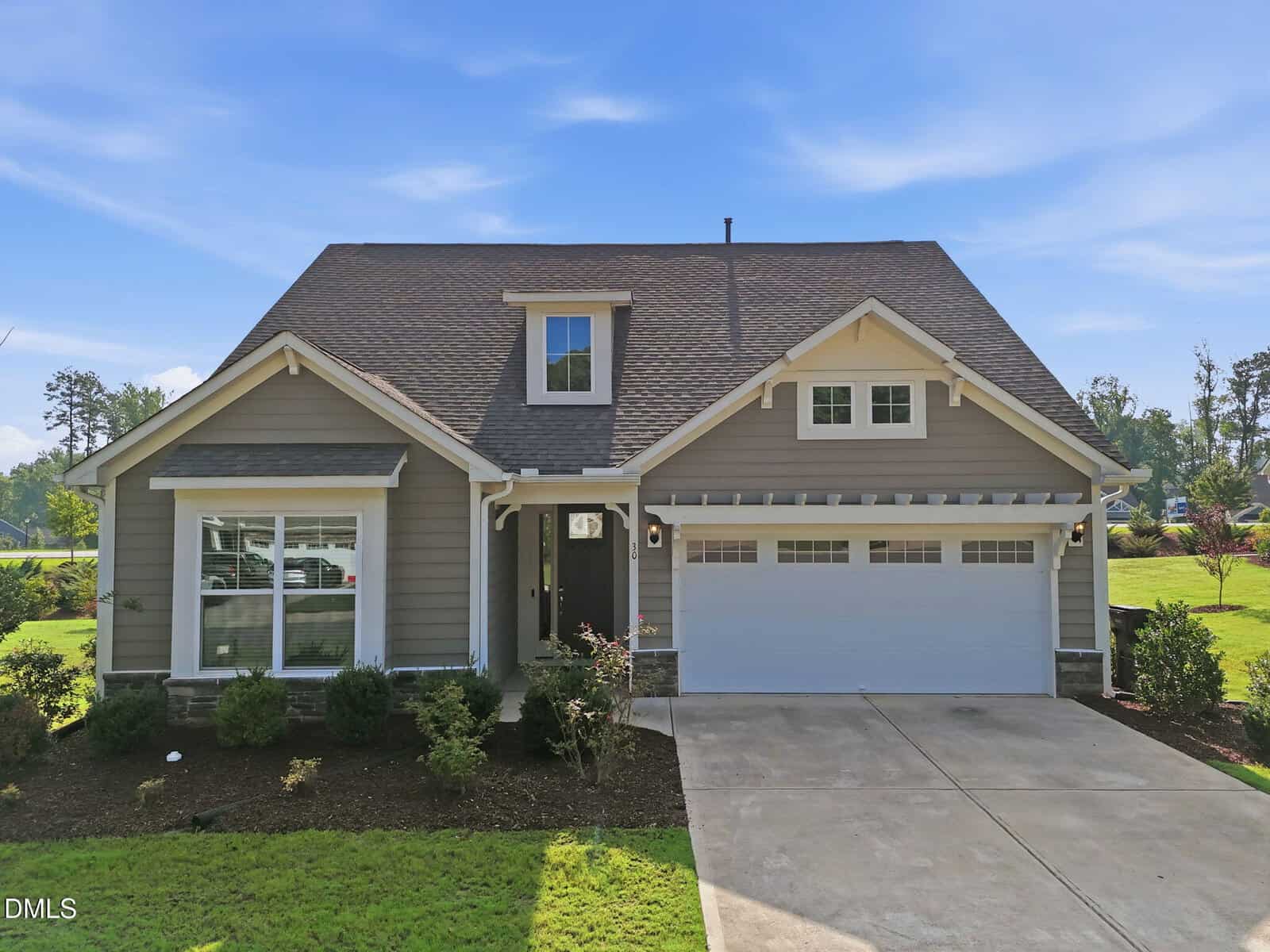 Single-story gray house with white trim, a front porch, two-car garage, gabled roof, and a neatly landscaped yard with shrubs and grass on a sunny day.