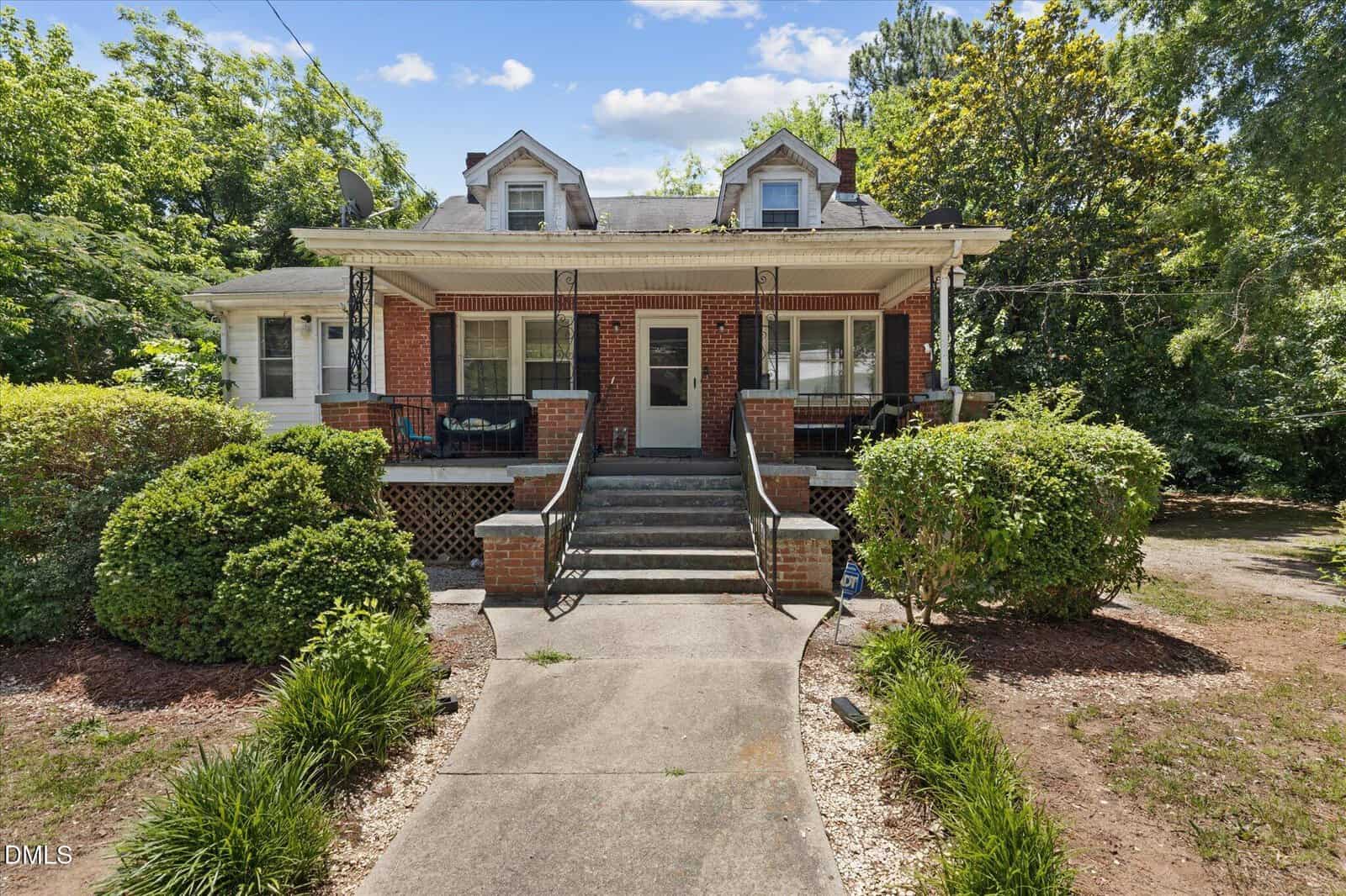 A brick house at 112 Peace Street, Oxford, features a large front porch, two dormer windows, central steps leading to the entrance with metal railings, and is surrounded by green bushes and trees on a sunny day.