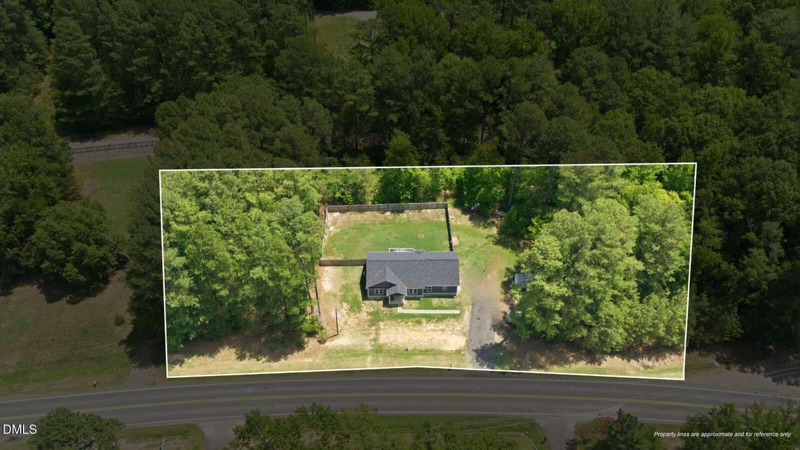 Aerial view of a single-story house surrounded by trees, with the property boundary highlighted. The house has a gray roof and sits near a road, with forested areas on all sides of the lot.