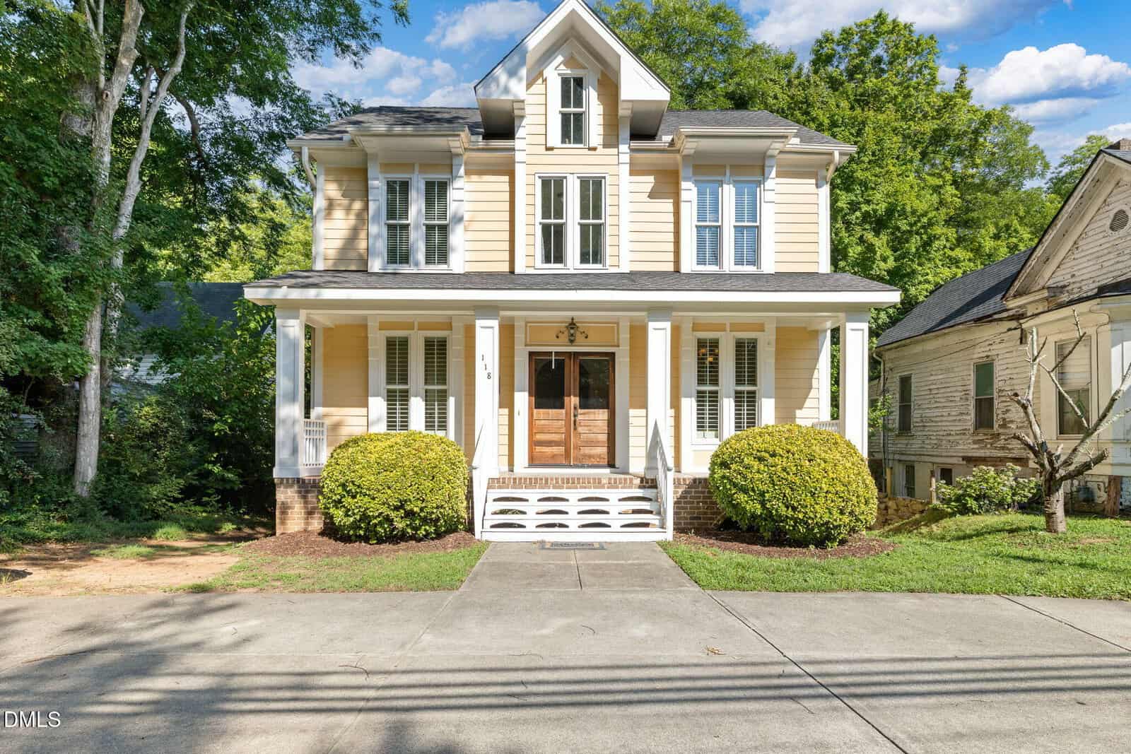 A two-story cream-colored house at 118 N Main Street, Franklinton, with a covered front porch, wooden double doors, and white trim. Bushes line the front, and a concrete driveway leads to the entrance. Trees and a neighboring house are visible.