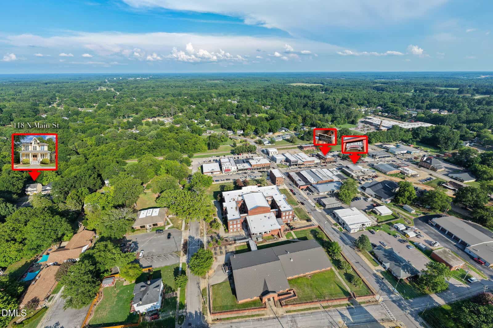 Aerial view of a green town with roads and buildings. Four buildings are highlighted with red boxes and labels. Trees and open sky are visible in the background.