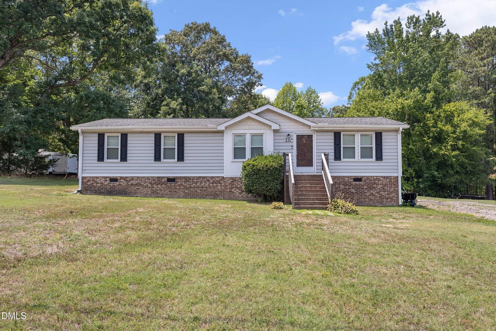 Single-story house with white siding and brick base, black shutters, front steps, and a small bush by the entrance. Located at 291 Cooke Road in Louisburg, this home is surrounded by a large grassy yard and trees in the background under a partly cloudy sky.