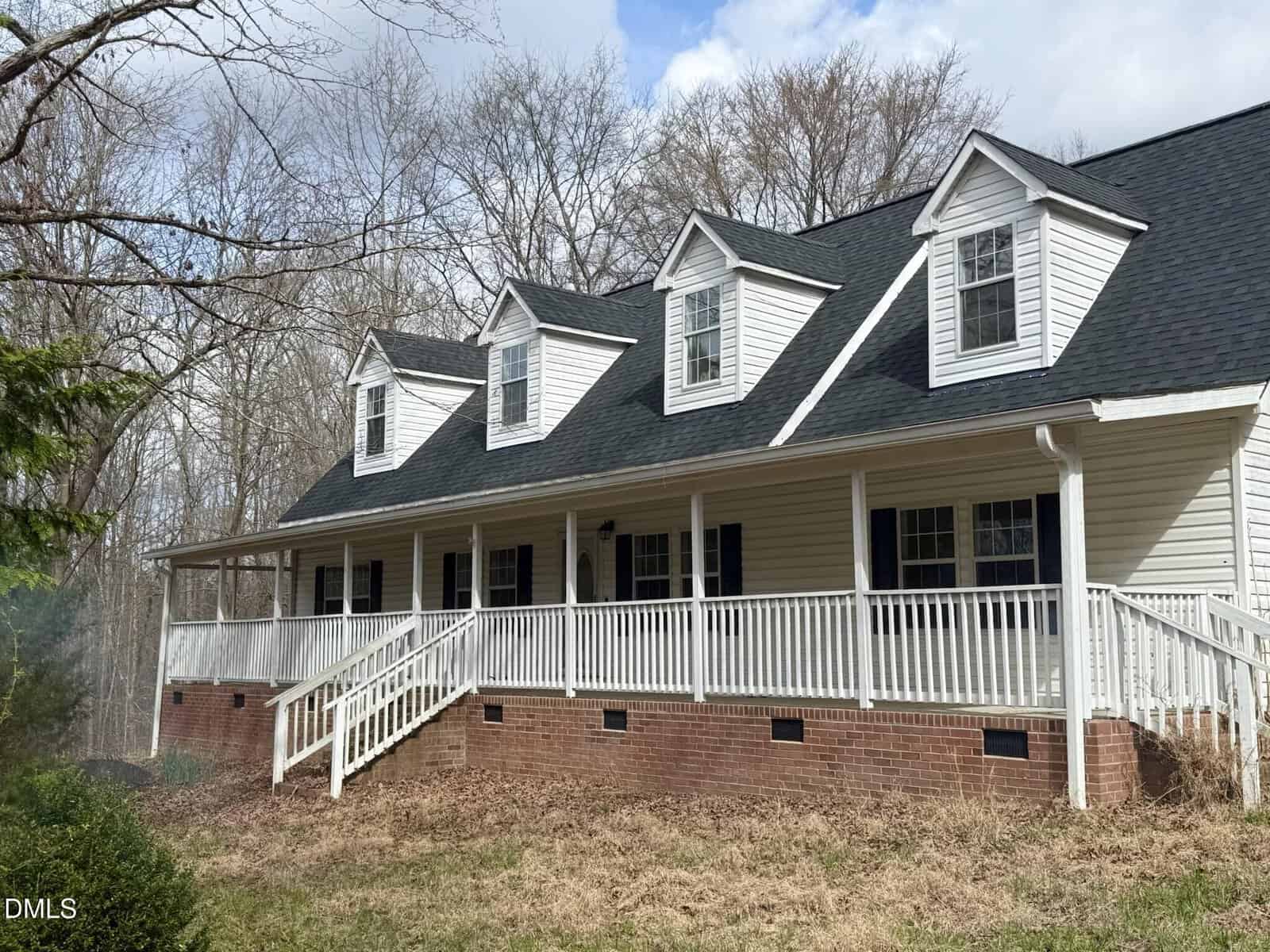A white, two-story house on 5019 Dorsey Road with three dormer windows, a black roof, and a large front porch with white railings, set against a backdrop of leafless trees and cloudy Oxford sky.