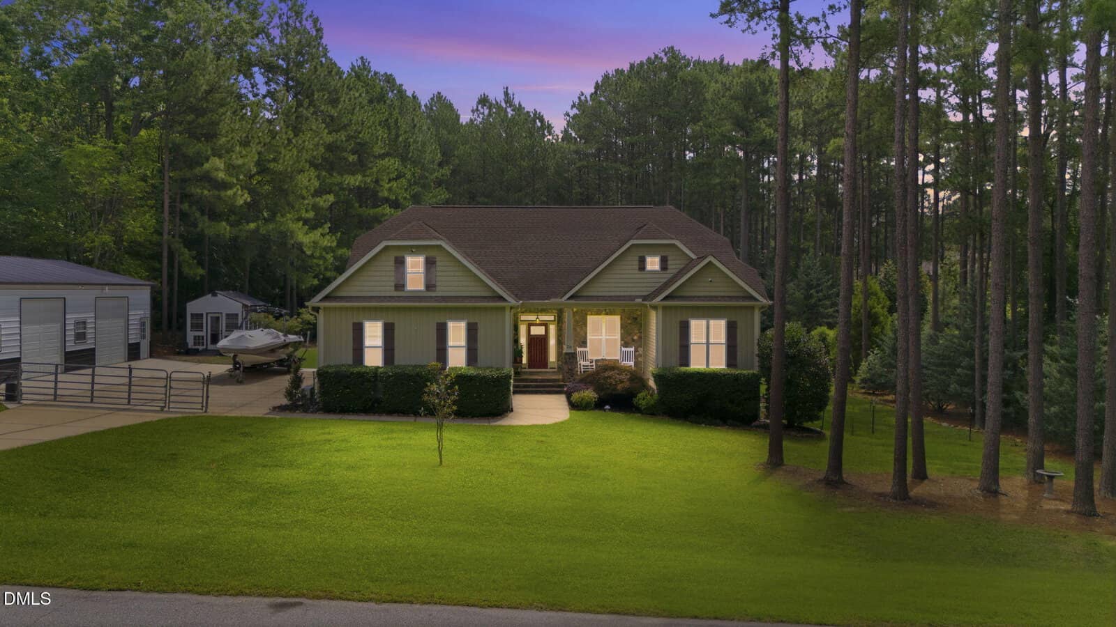 Green single-story house with a front porch, well-kept lawn, and surrounding trees at dusk on 20 Torrance Way in Youngsville. A paved driveway leads to a parked boat and a shed in the background. The sky shows a purple-blue sunset.