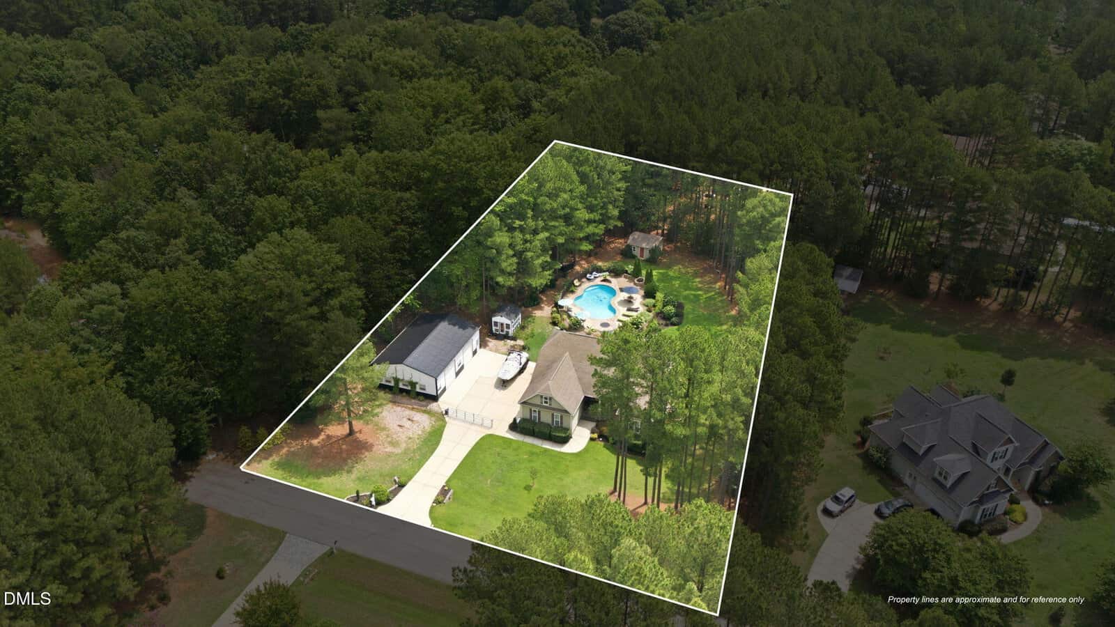 Aerial view of a wooded property outlined in white, featuring a house, detached building, driveway, and a backyard pool, surrounded by dense trees and neighboring homes.