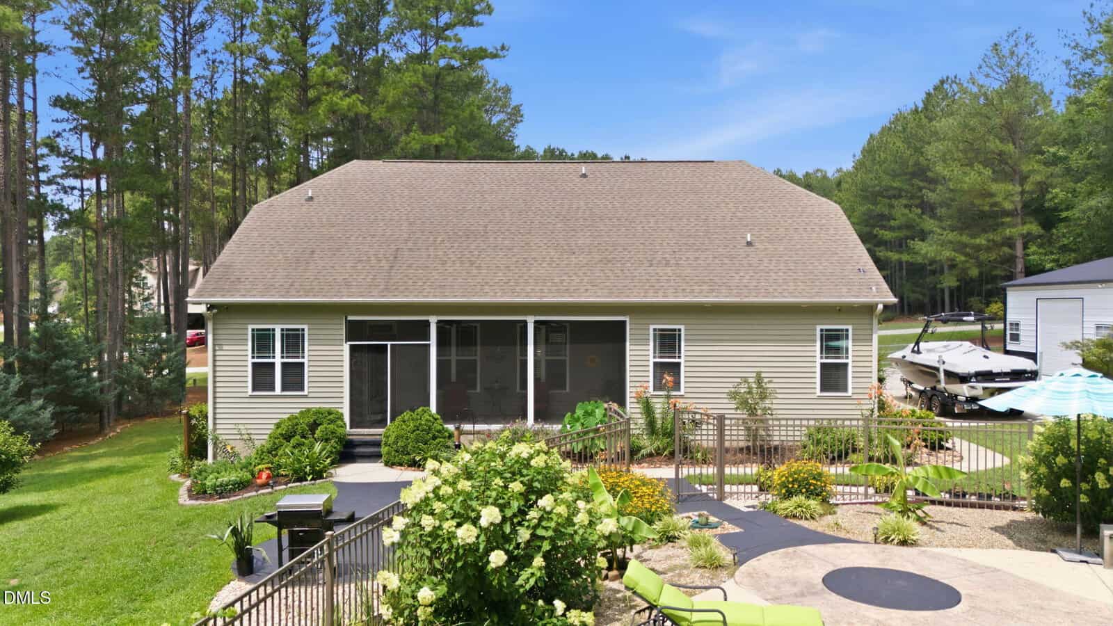 A beige house with a screened porch, surrounded by landscaped gardens. A patio, grill, and pool with an umbrella are in the backyard. Trees and a boat on a trailer are visible to the right.