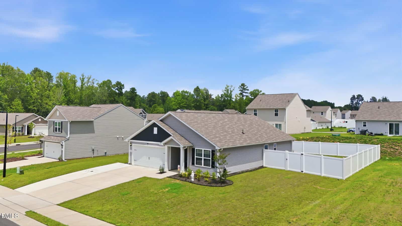 Single-story gray house with a two-car garage, fenced backyard, and well-kept lawn in a suburban neighborhood with similar homes, trees in the background, and a clear blue sky above.