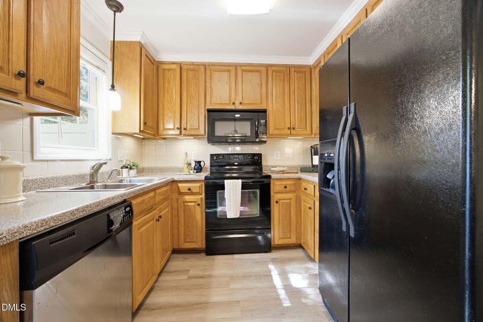 Kitchen with wooden cabinets, black appliances, double sink, dishwasher, and granite countertops. Bright window above the sink lets in natural light, creating a warm and inviting atmosphere.