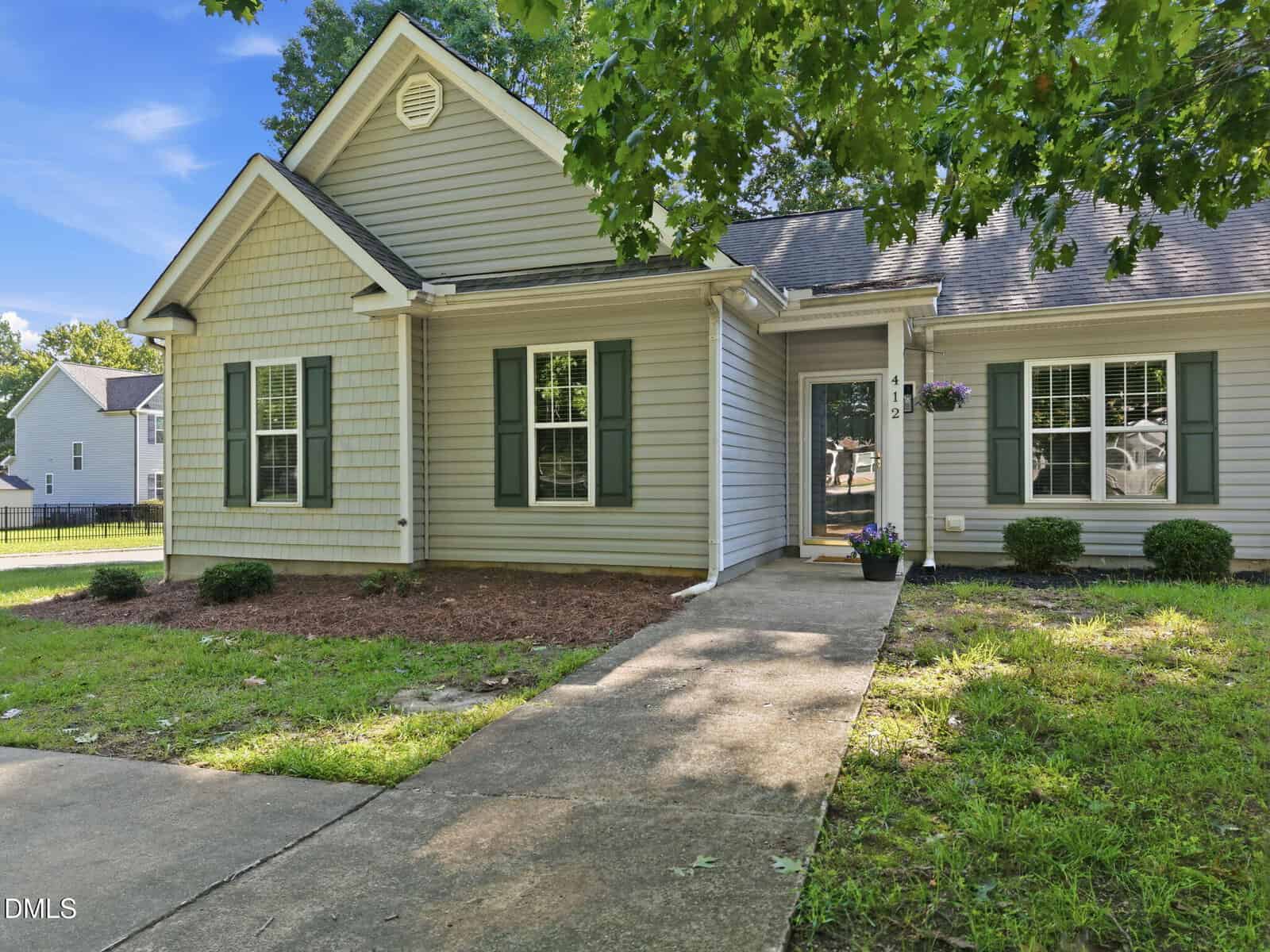 A single-story house at 412 N College Street in Youngsville features light gray siding, green shutters, and a covered entryway. A concrete walkway leads to the front door, surrounded by shrubs and a tree in the well-kept front yard.