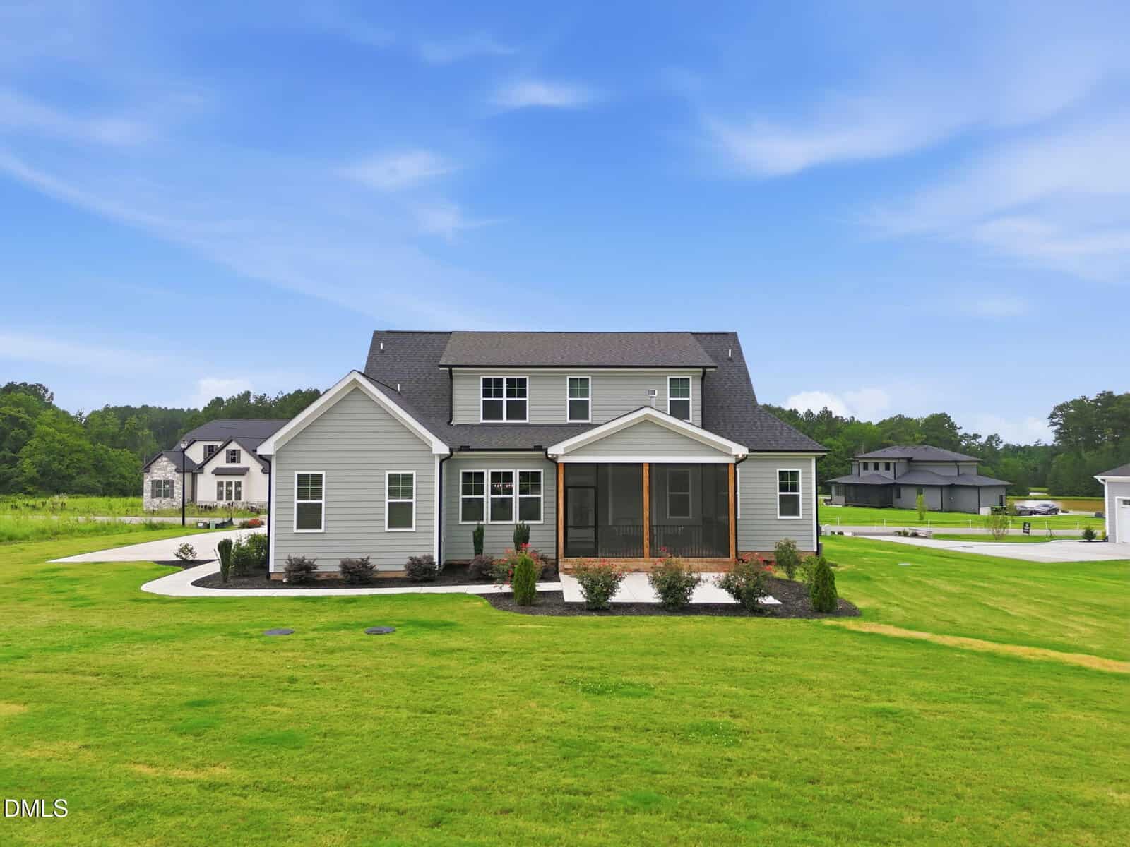 A two-story modern house with gray siding, large windows, and a screened porch sits on a spacious green lawn under a partly cloudy blue sky. Other homes and trees are visible in the background.