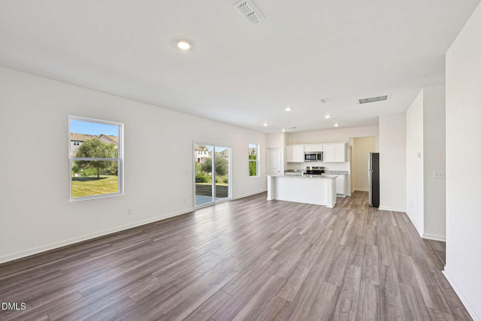 Spacious open-concept home with light wood floors, white walls, large windows, sliding glass doors, and a modern kitchen featuring white cabinets, stainless steel appliances, and an island.