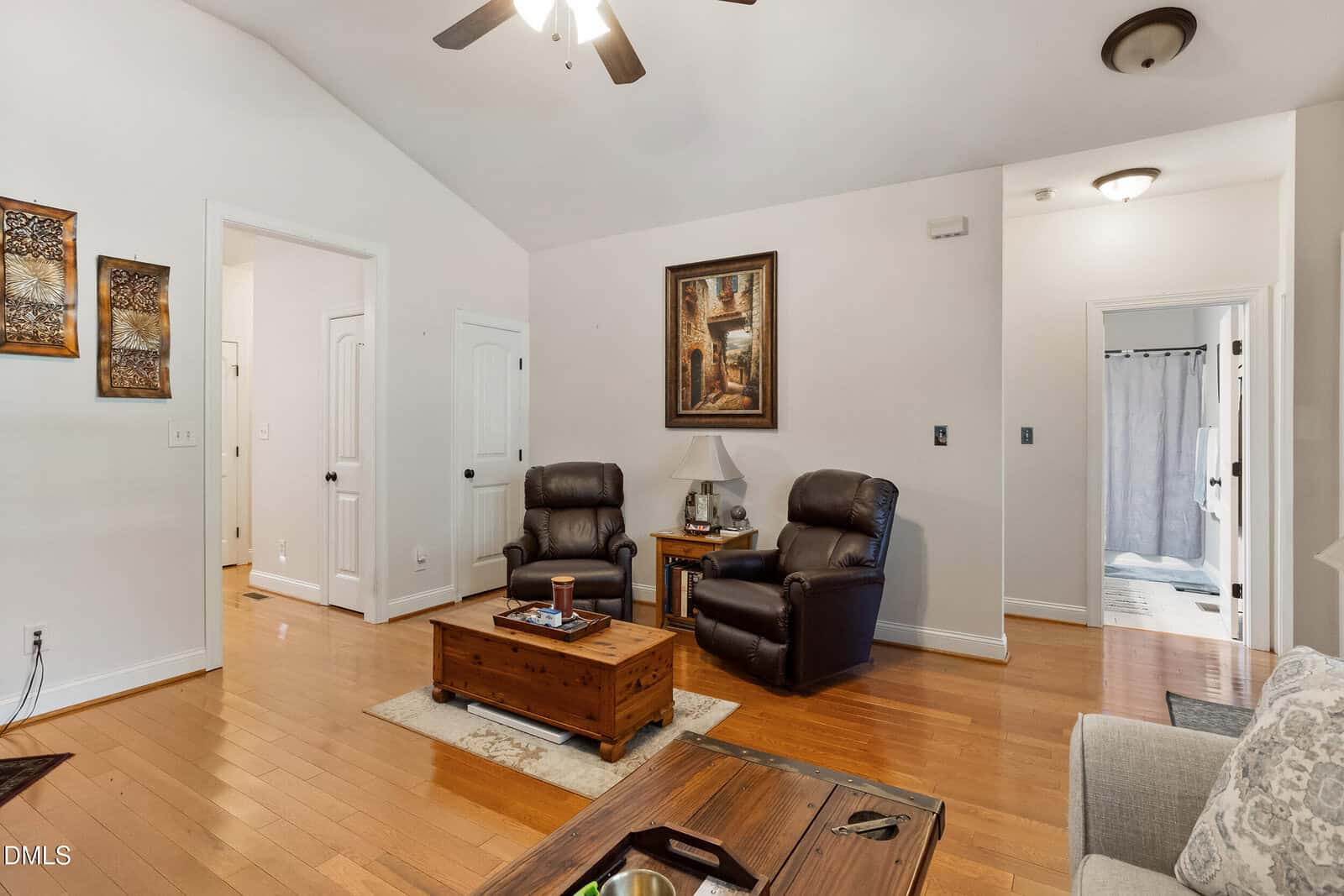 Living room with two dark recliners, a wooden coffee table, wall art, and hardwood floors. Hallways and doors lead to other rooms; a ceiling fan and light fixtures are visible above.