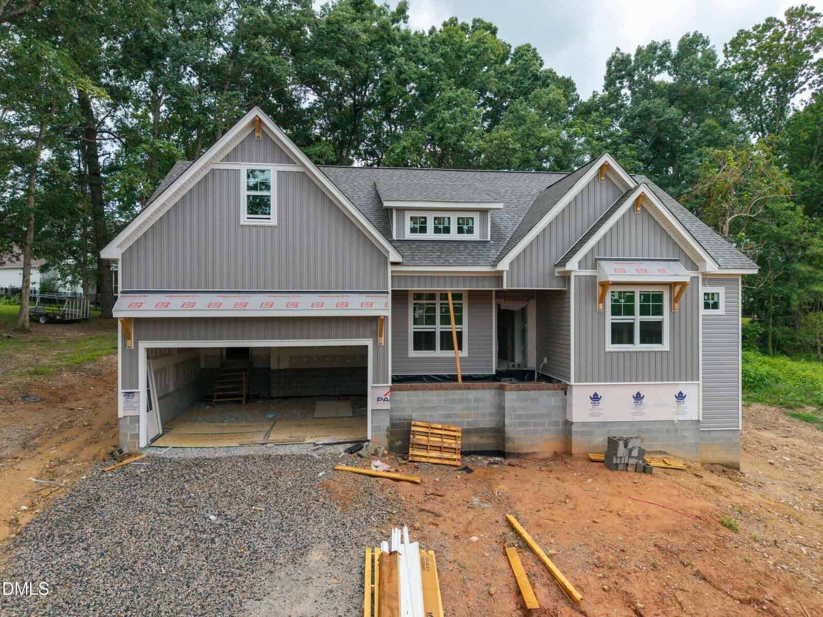 This newly constructed house at 1039 Heather Lane in Wake Forest features gray siding, white trim, and a spacious two-car garage. The yard currently contains dirt and construction materials, with trees providing a natural backdrop. The home appears unfinished.