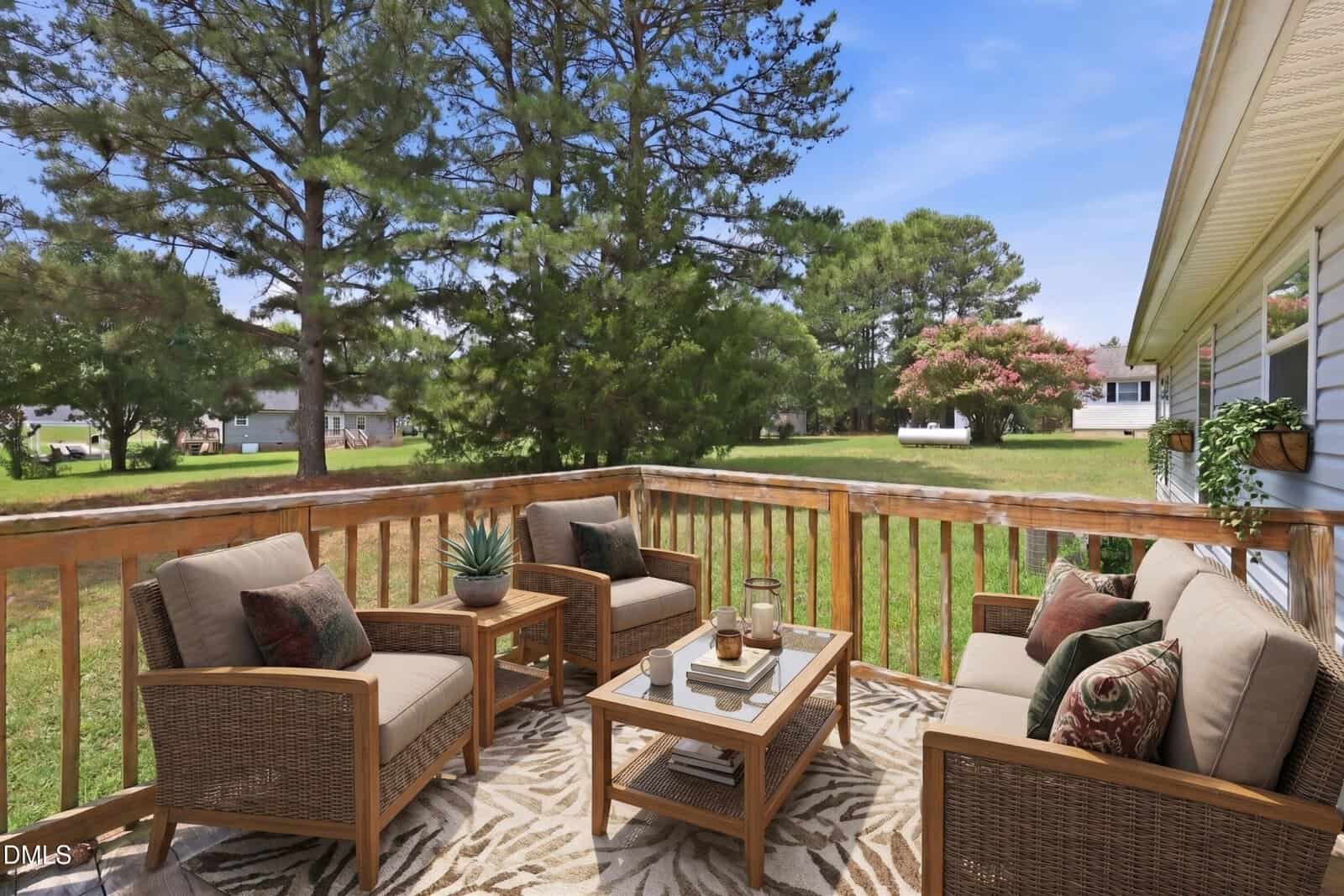 A cozy patio with cushioned seating and a glass coffee table overlooks a grassy backyard with trees. The area rug adds a comfortable touch to the outdoor setting.