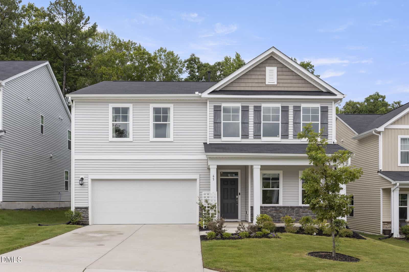 Two-story suburban house at 65 Carolina Maple Drive, Franklinton, with gray siding, white trim, a covered front porch, double garage, and landscaped front yard, set against a backdrop of trees under a blue sky.
