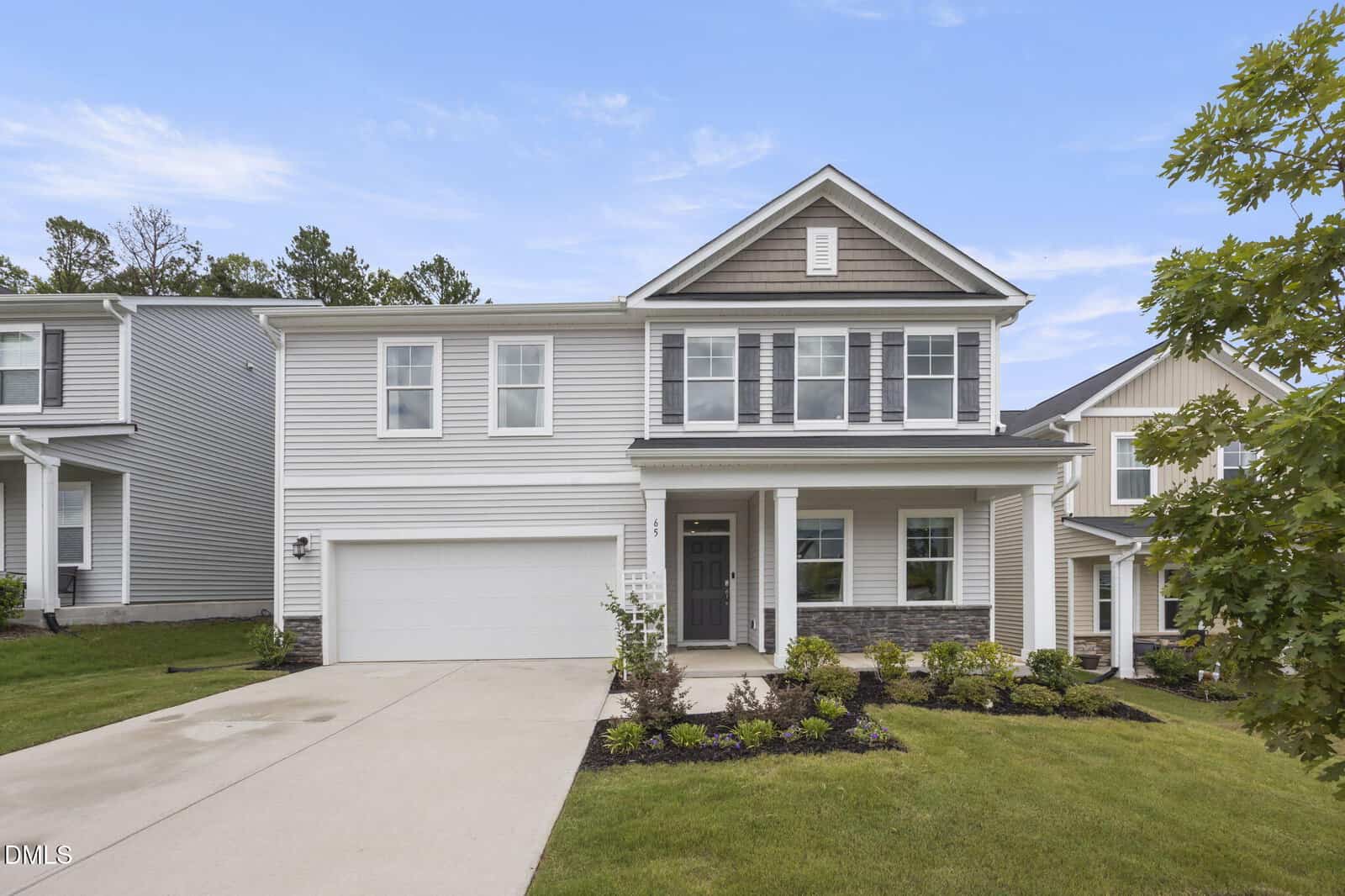 Two-story modern suburban house with gray siding, attached two-car garage, covered front porch, landscaped yard, and a concrete driveway on a sunny day.