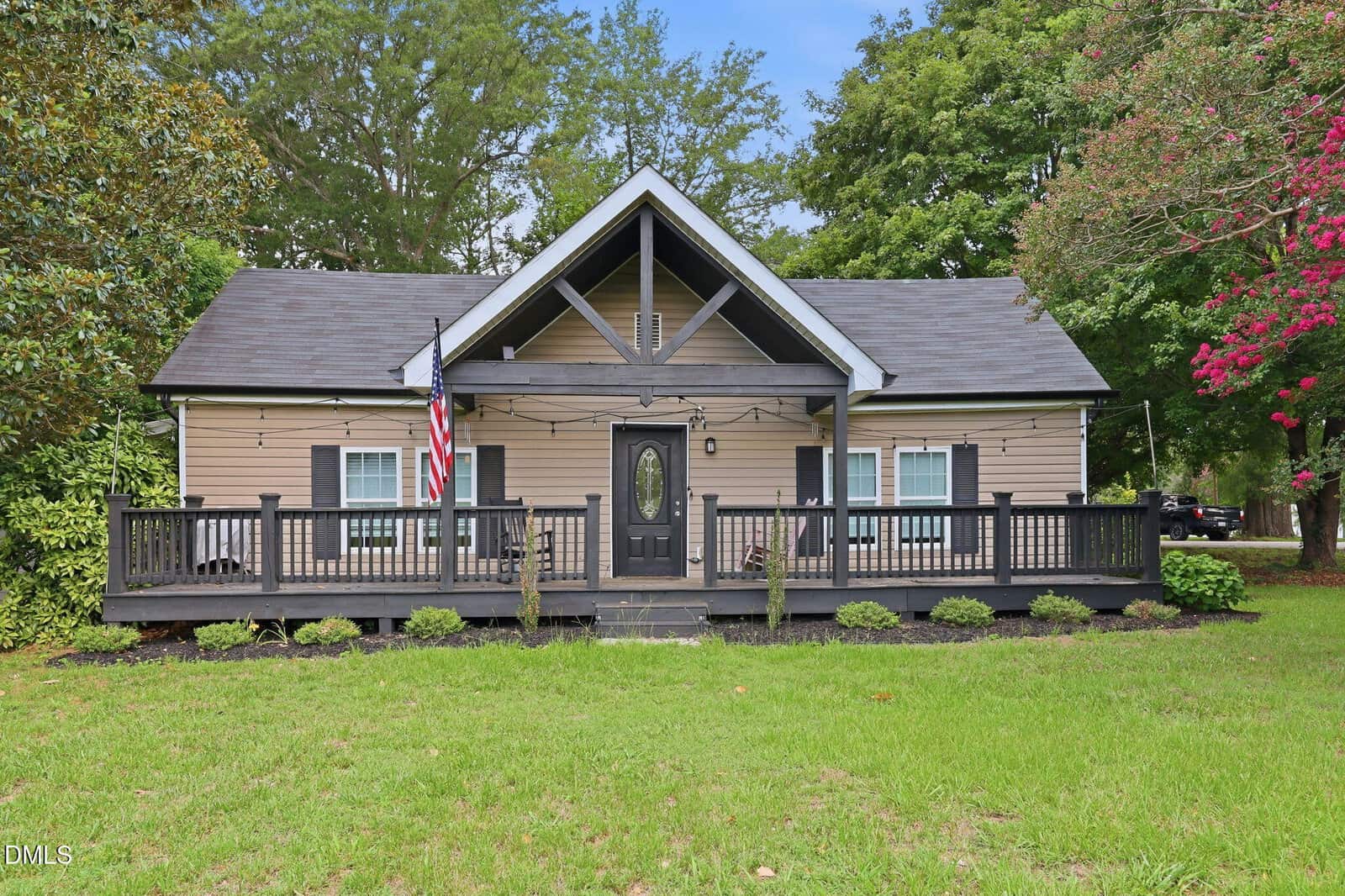 Single-story tan house with black trim, front porch, and gabled roof at 33 American Legion Road, Franklinton. An American flag hangs near the steps. The yard is grassy with some shrubs and large trees surrounding the house.