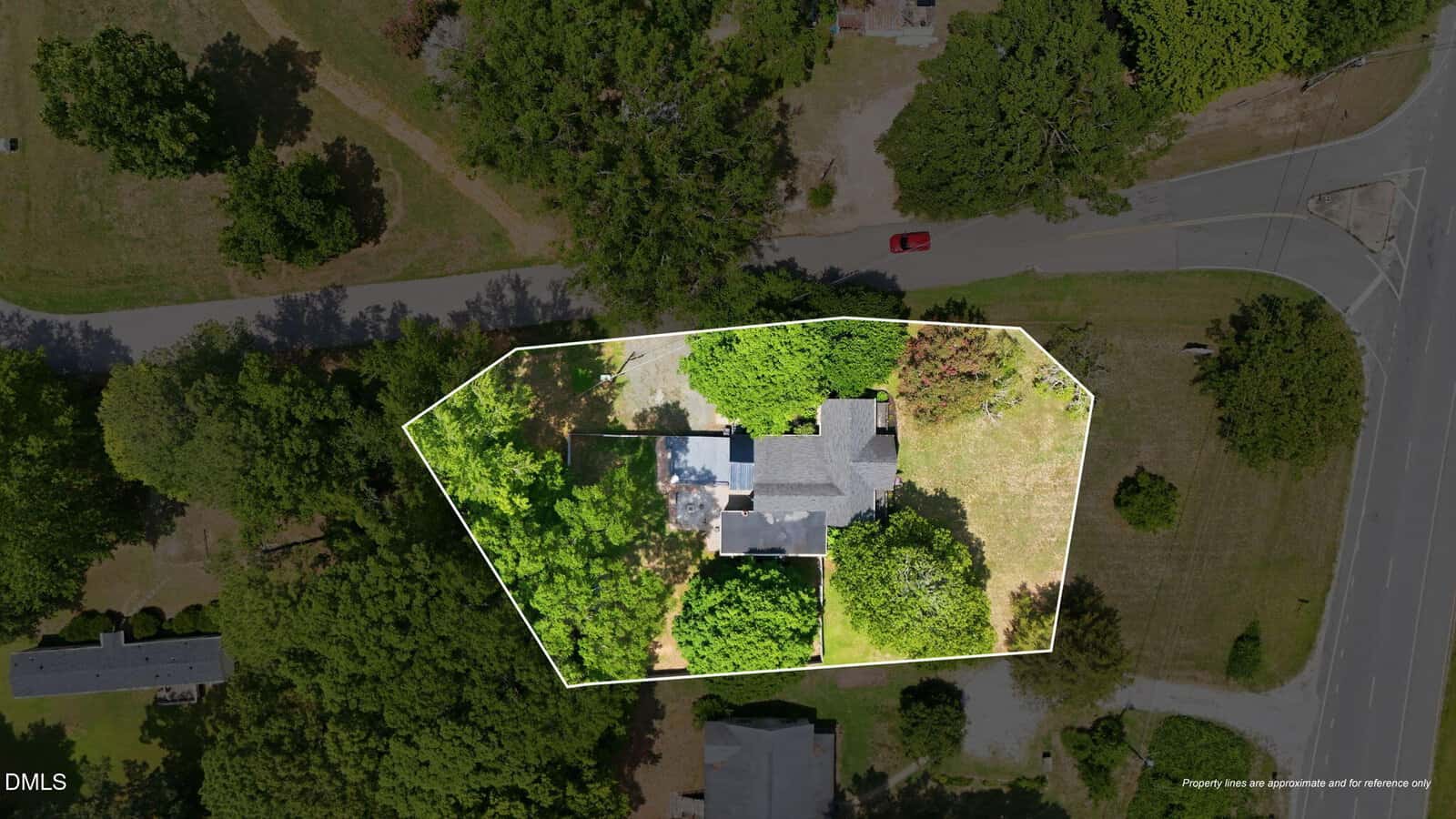 Aerial view of a house and yard outlined in white, surrounded by trees and greenery, with roads on two sides and neighboring homes nearby.