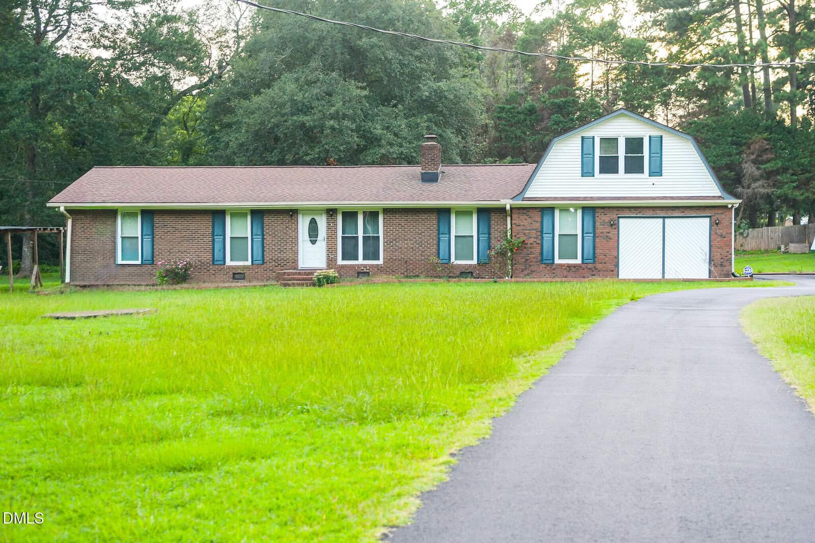 Single-story brick house with blue shutters, a garage, and an upstairs room, surrounded by green grass and trees on 152 N C 39 Loop Road in Henderson. A paved driveway curves to the front entrance.