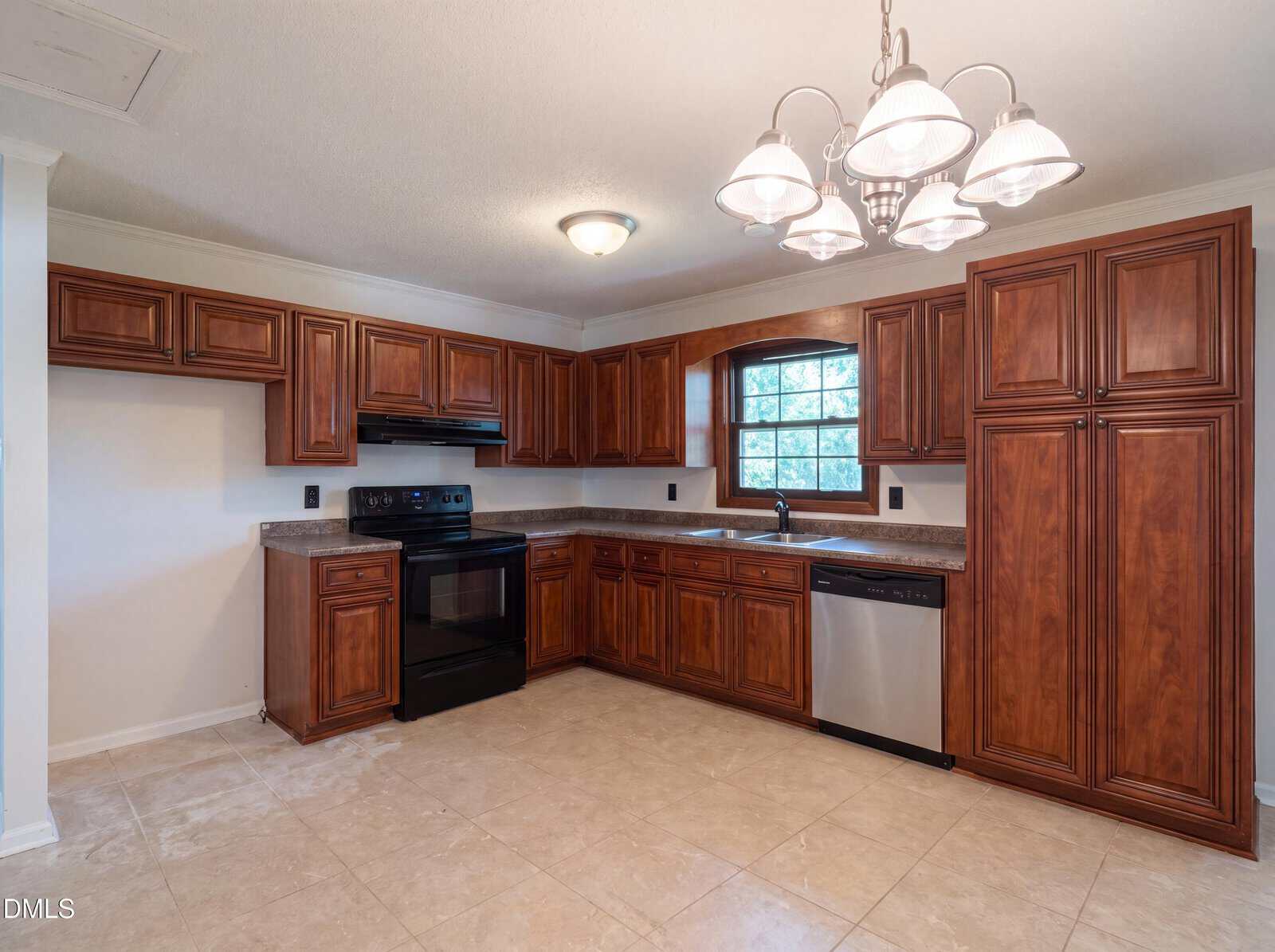 Kitchen with dark wood cabinets, black stove and microwave, stainless steel dishwasher, beige tile floor, and a window above the sink; chandelier lights hang from the ceiling.