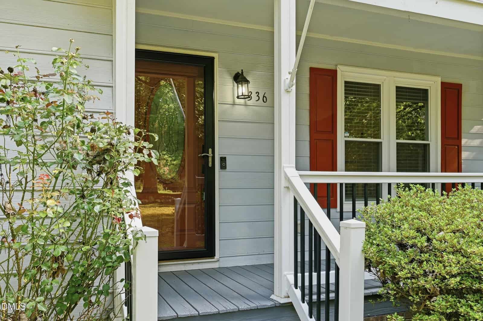 Front porch of a house at 336 Thornwood Lane in Youngsville with light blue siding, red shutters, a glass front door, and white railings. There are bushes and greenery near the steps, and the house number 36 is visible by the door.