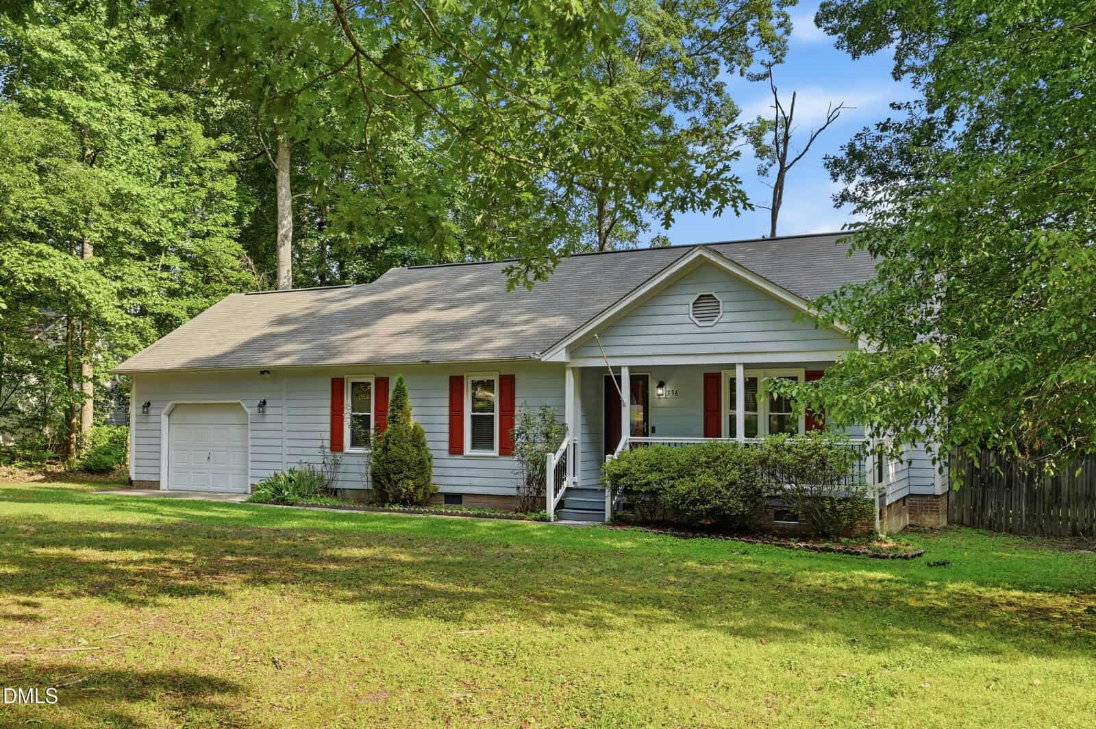 Single-story gray house with red shutters, front porch, and attached garage, surrounded by green trees and lawn on a sunny day.