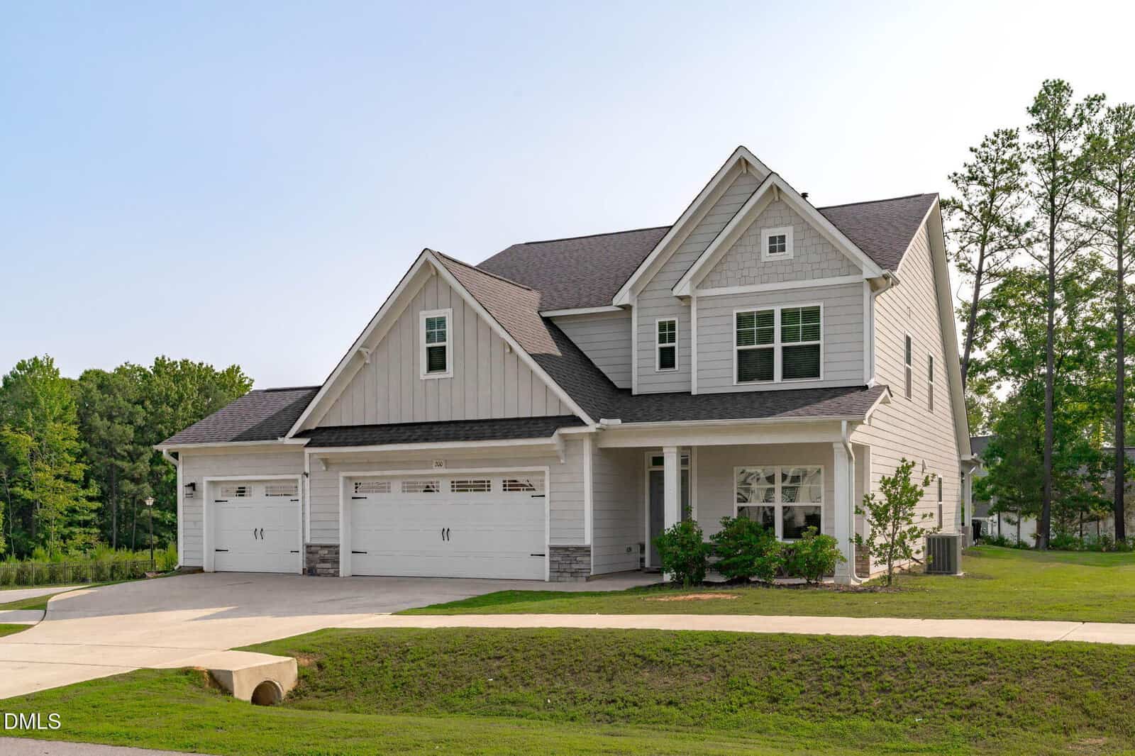 A modern two-story suburban house at 200 Sutherland Drive in Franklinton features light gray siding, three white garage doors, a dark shingle roof, and a well-kept lawn, all surrounded by trees and clear skies.
