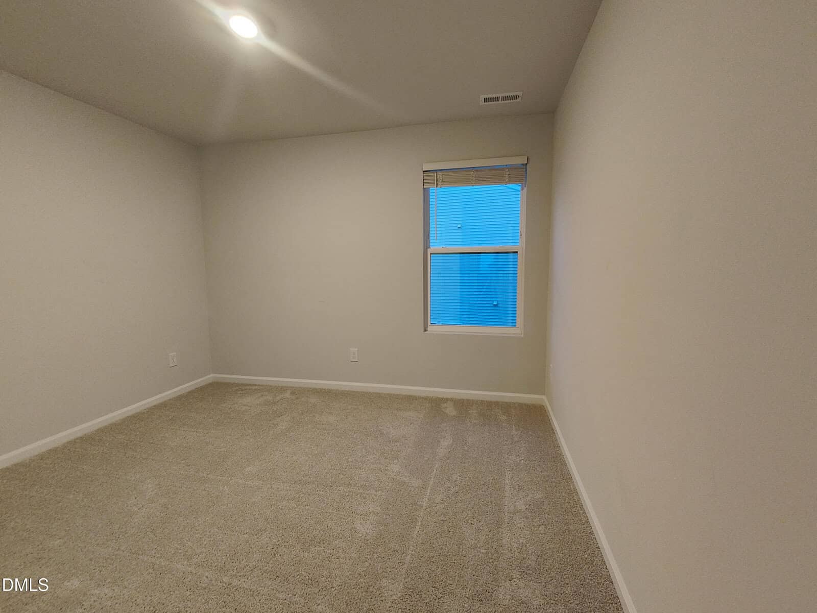Empty room with beige carpet, off-white walls, a single window with blinds, and a ceiling light. The room appears clean and ready for furnishing.
