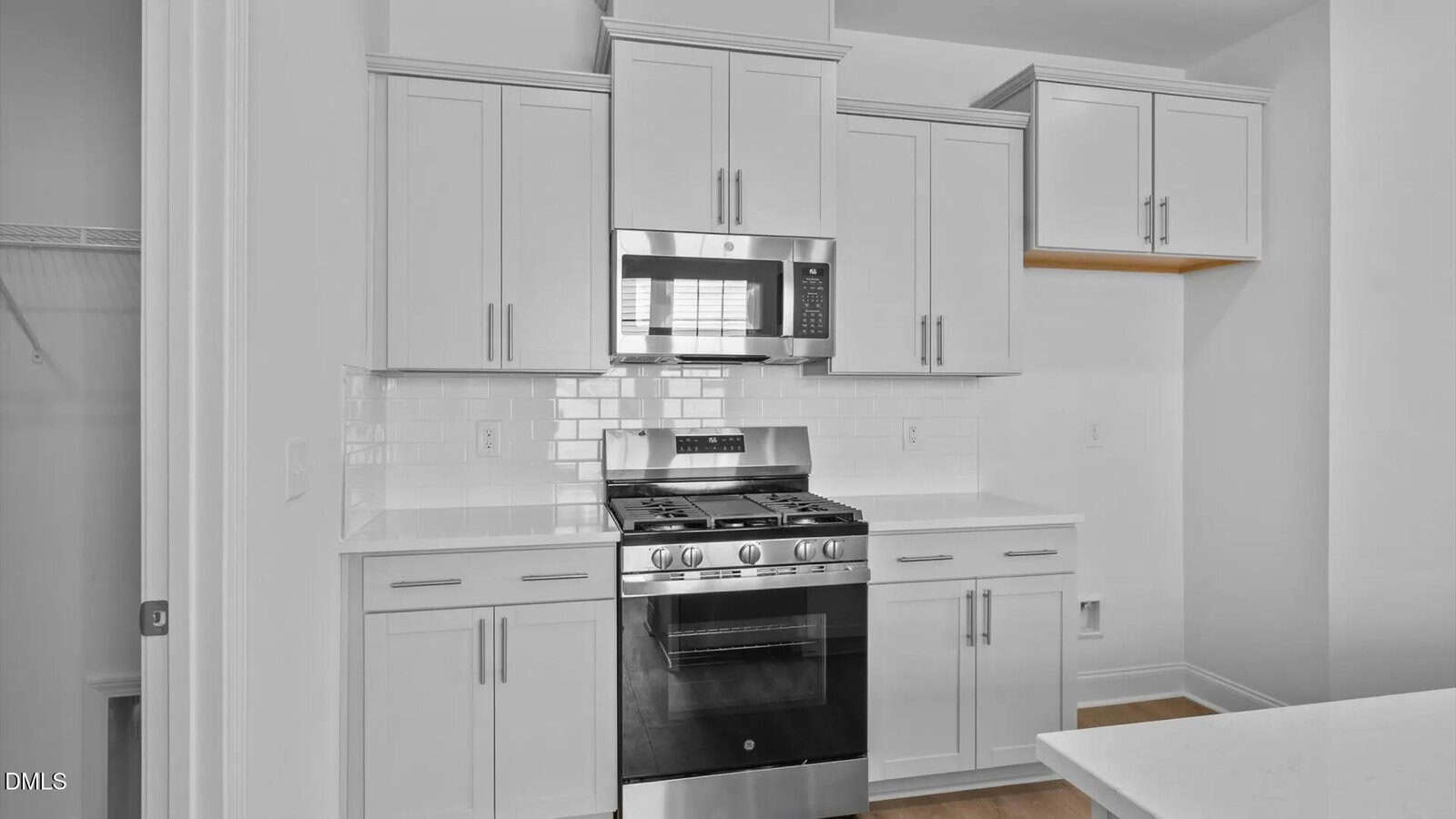 Modern white kitchen with shaker cabinets, stainless steel gas stove and microwave, white subway tile backsplash, and quartz countertops. Open shelving is visible in the upper right corner.