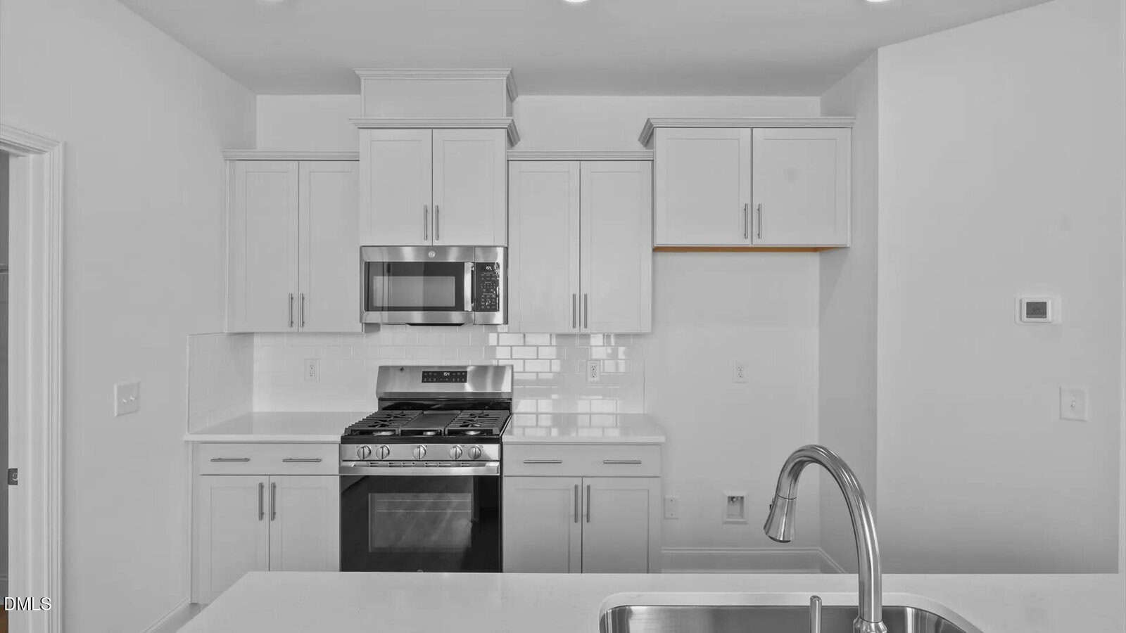 Modern kitchen with white cabinets, stainless steel appliances including a gas stove and microwave, a subway tile backsplash, and a sink with a curved faucet in the foreground.