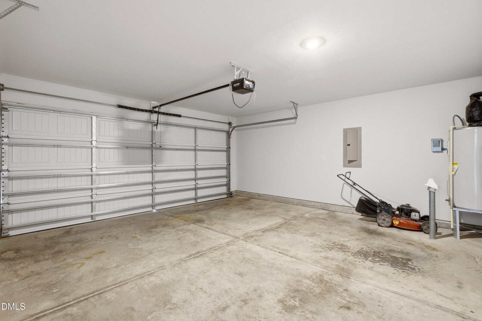 Clean, empty two-car garage with a concrete floor, automatic double garage door, overhead lighting, a water heater, and a lawnmower positioned against the right wall.