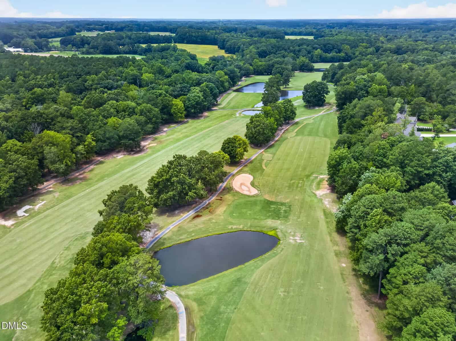 Aerial view of a green golf course with sand traps, ponds, and trees surrounding the fairways on a sunny day.