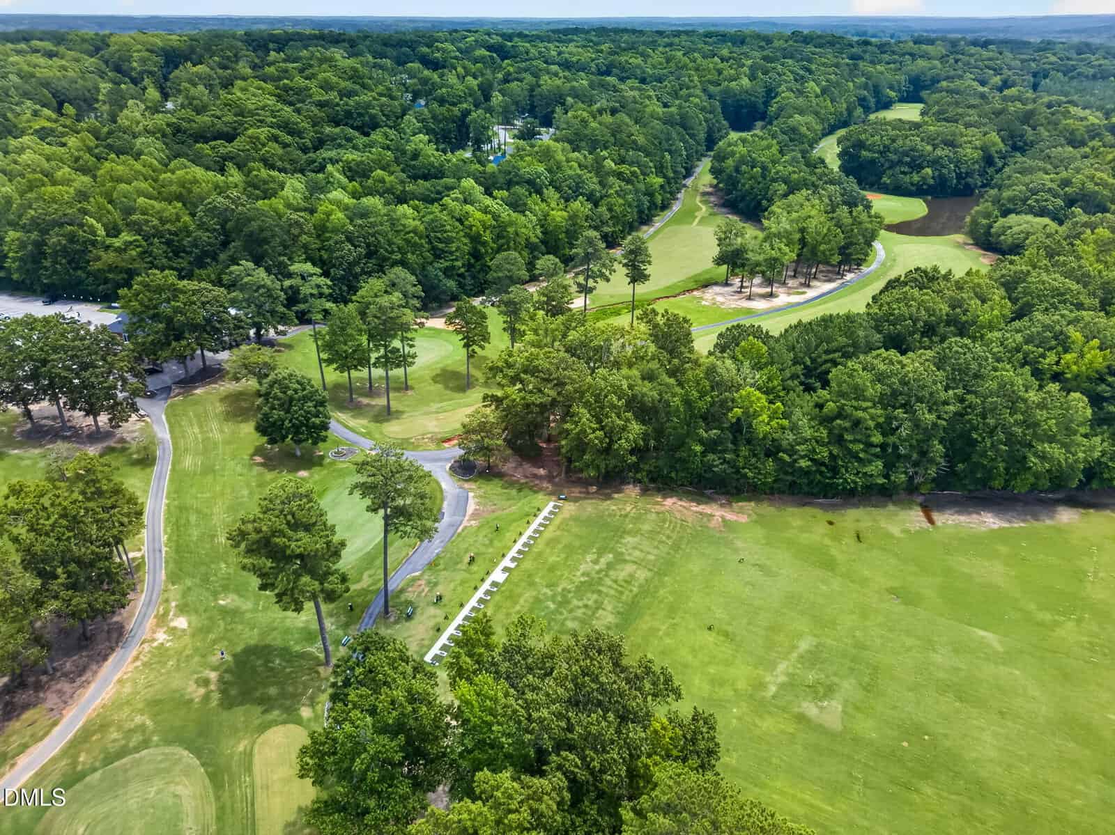 Aerial view of a lush golf course with winding paths, sand traps, and dense green trees surrounding open grassy fairways.