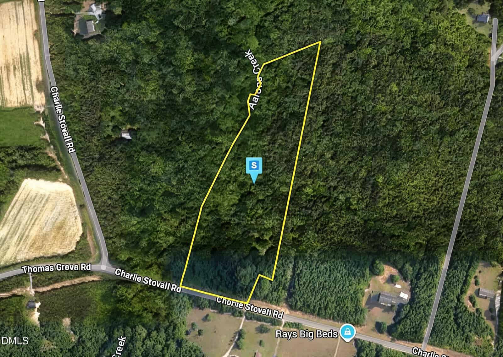 Aerial view of a wooded property outlined in yellow with a creek running through it, bordered by Charlie Stovall Rd and Thomas Greva Rd near 8438 Charlie Stovall Road, Oxford. A few houses and fields are nearby. A blue icon marked "S" is near the center.