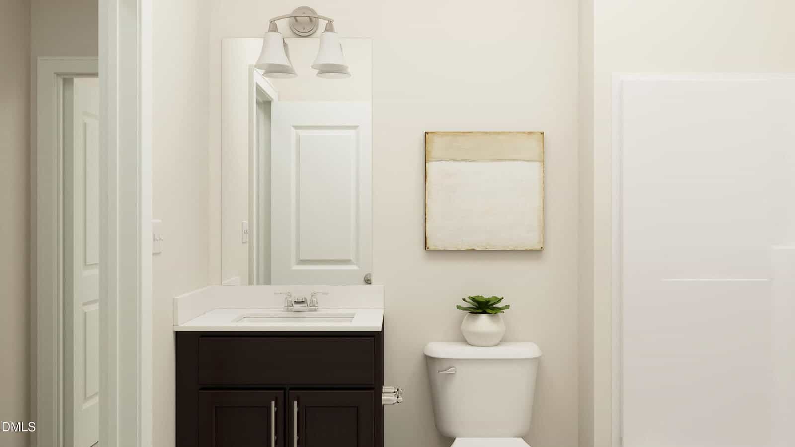 A modern bathroom with a white sink, dark vanity, wall mirror, toilet with a potted plant, abstract wall art, and a glass shower on the right side. The walls are light-colored, creating a clean and minimal look.