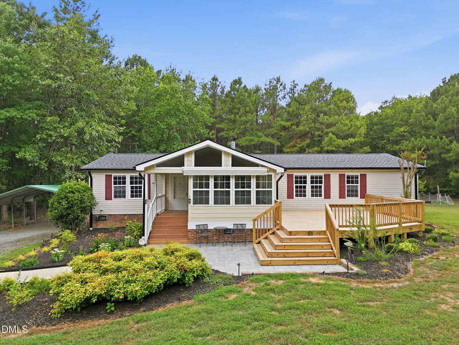 A single-story house at 7569 NC 96, Oxford, features beige siding, red shutters, a front porch with steps and a ramp, landscaped bushes, and trees in the background under a clear blue sky.