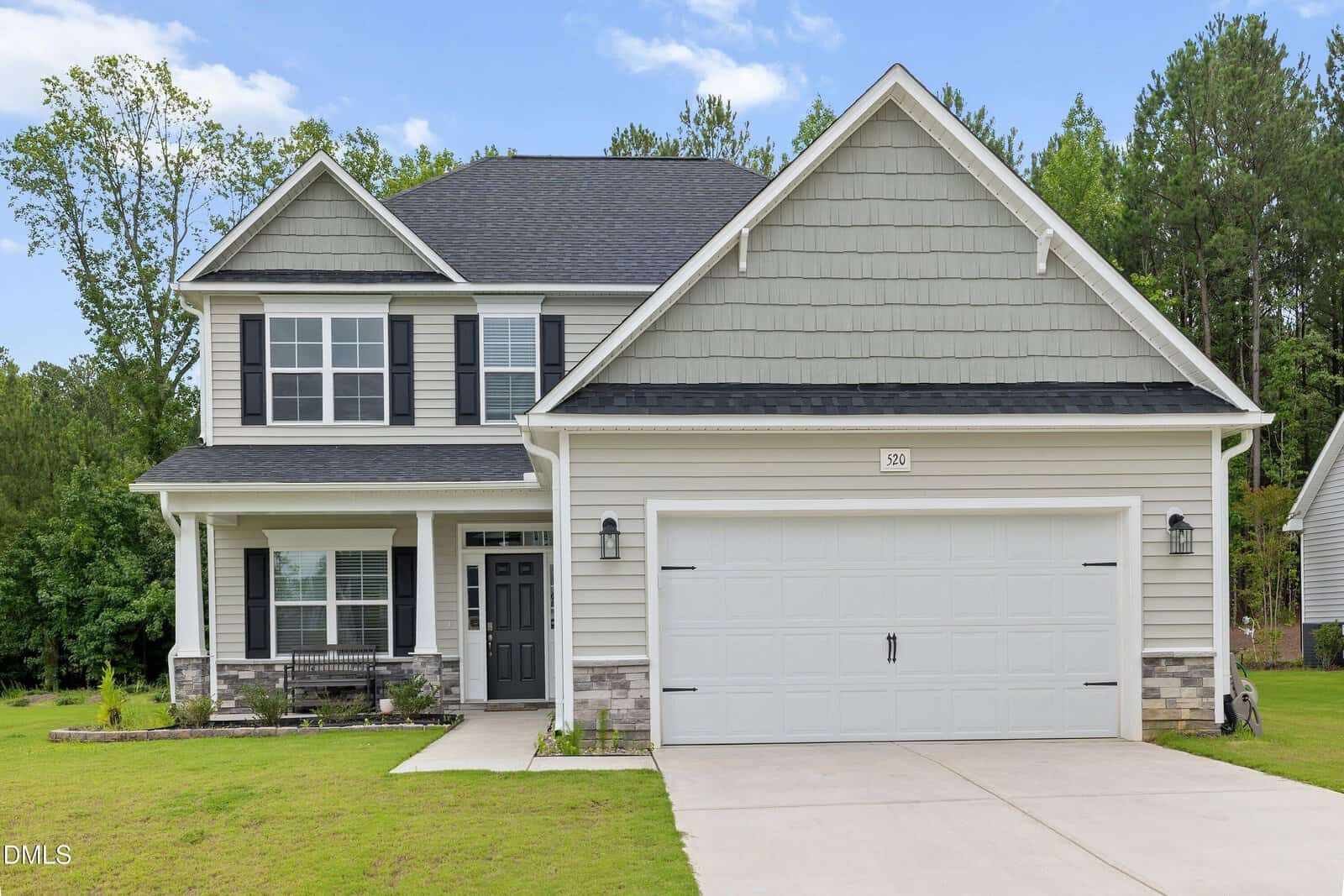 Two-story suburban house with gray siding, black shutters, a white garage door, and a covered front porch. Located at 520 Husketh Road in Youngsville, this home is set on a green lawn with trees in the background and a clear sky overhead.