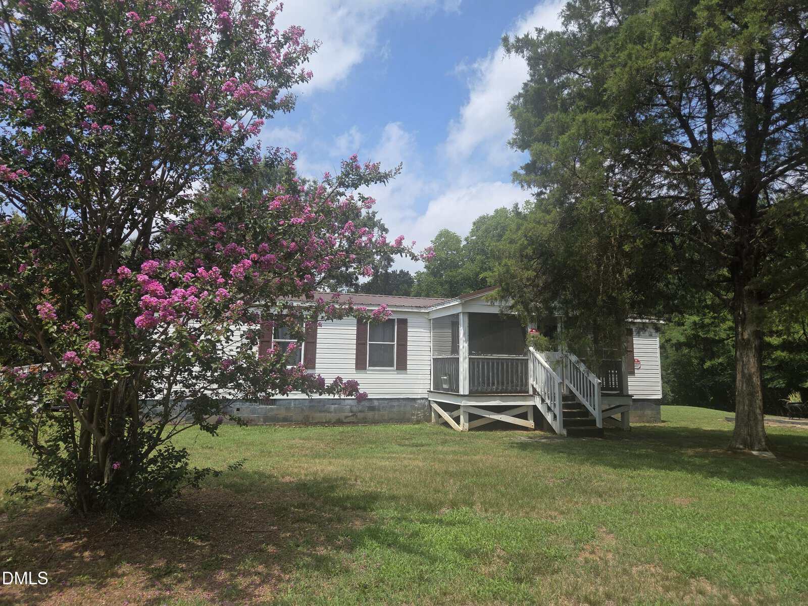 A white single-story house at 109 Bolton Lane in Warrenton features a charming front porch and stairs, surrounded by green trees and flowering pink bushes, all set beneath a partly cloudy sky.